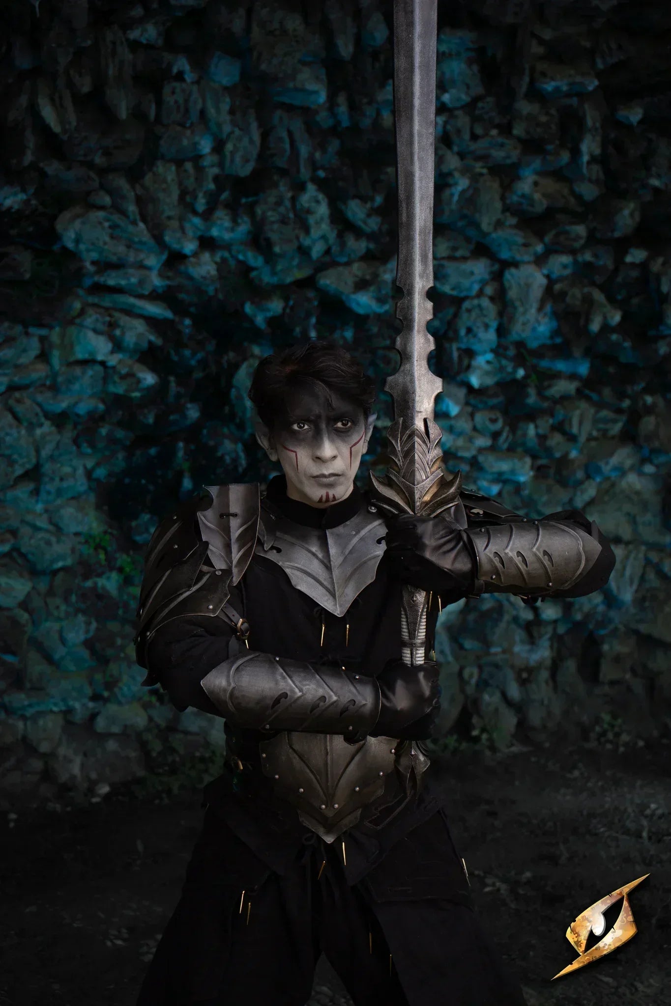 Cosplayer dressed as a dark warrior holding a sword, set against a stone wall background, embodying the theme of Eventide.