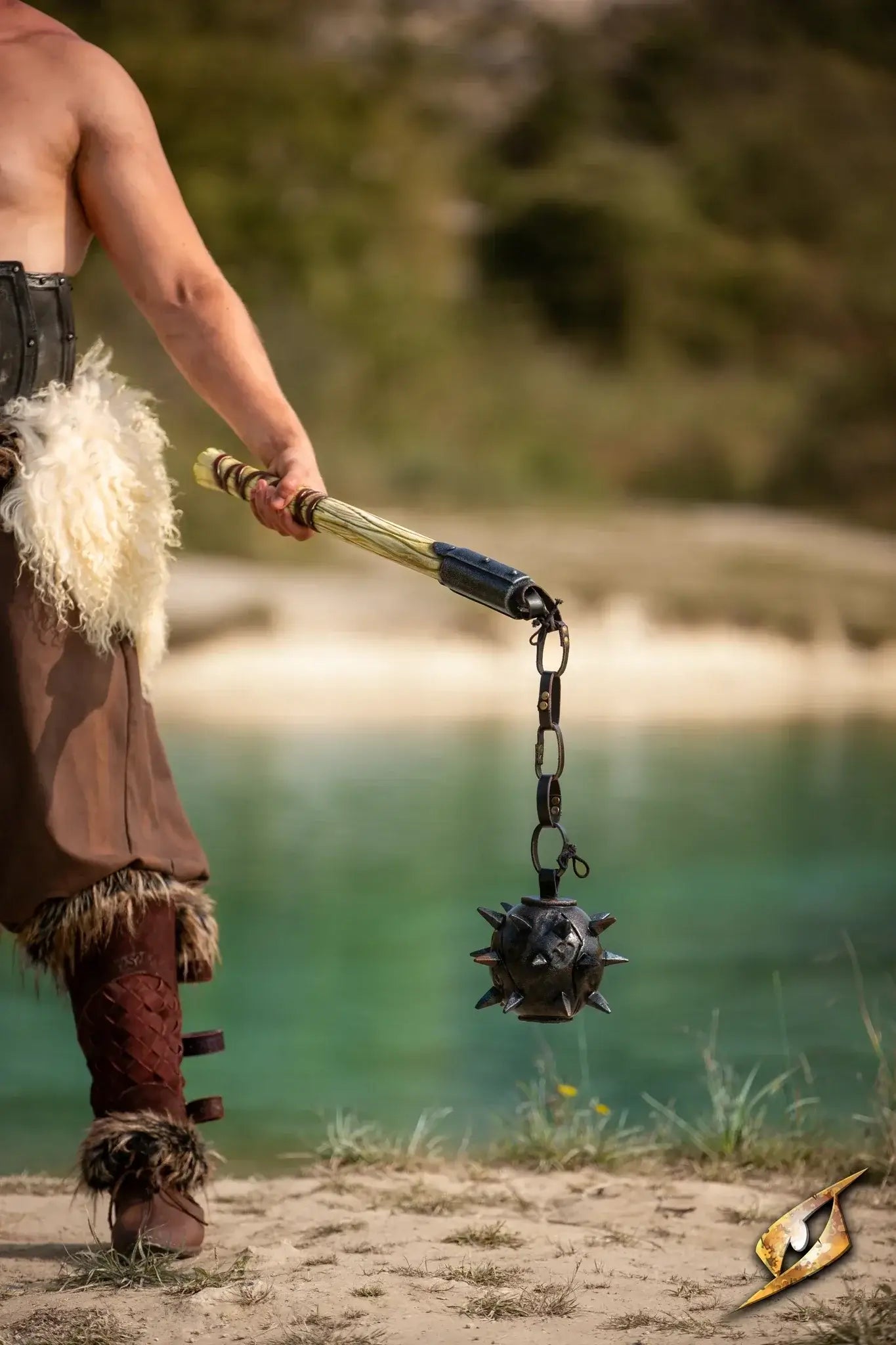 A warrior holding a spiked flail near a tranquil body of water.