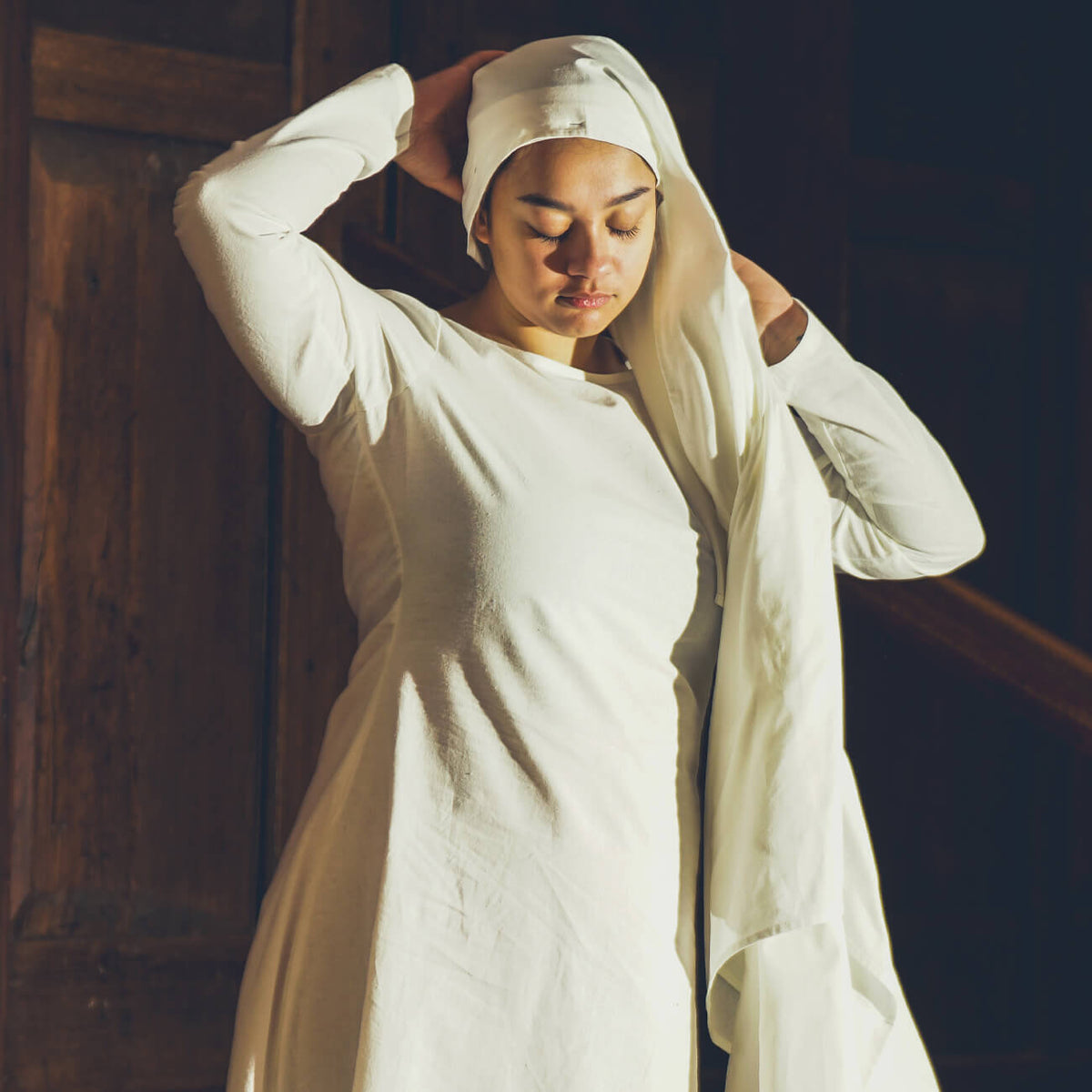 Medieval Undergarments - Yoremade woman putting on a white headscarf with medieval undergarment attire.