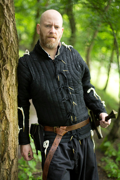Man wearing a gambeson standing by a tree, showcasing the essential gear for adventurers.