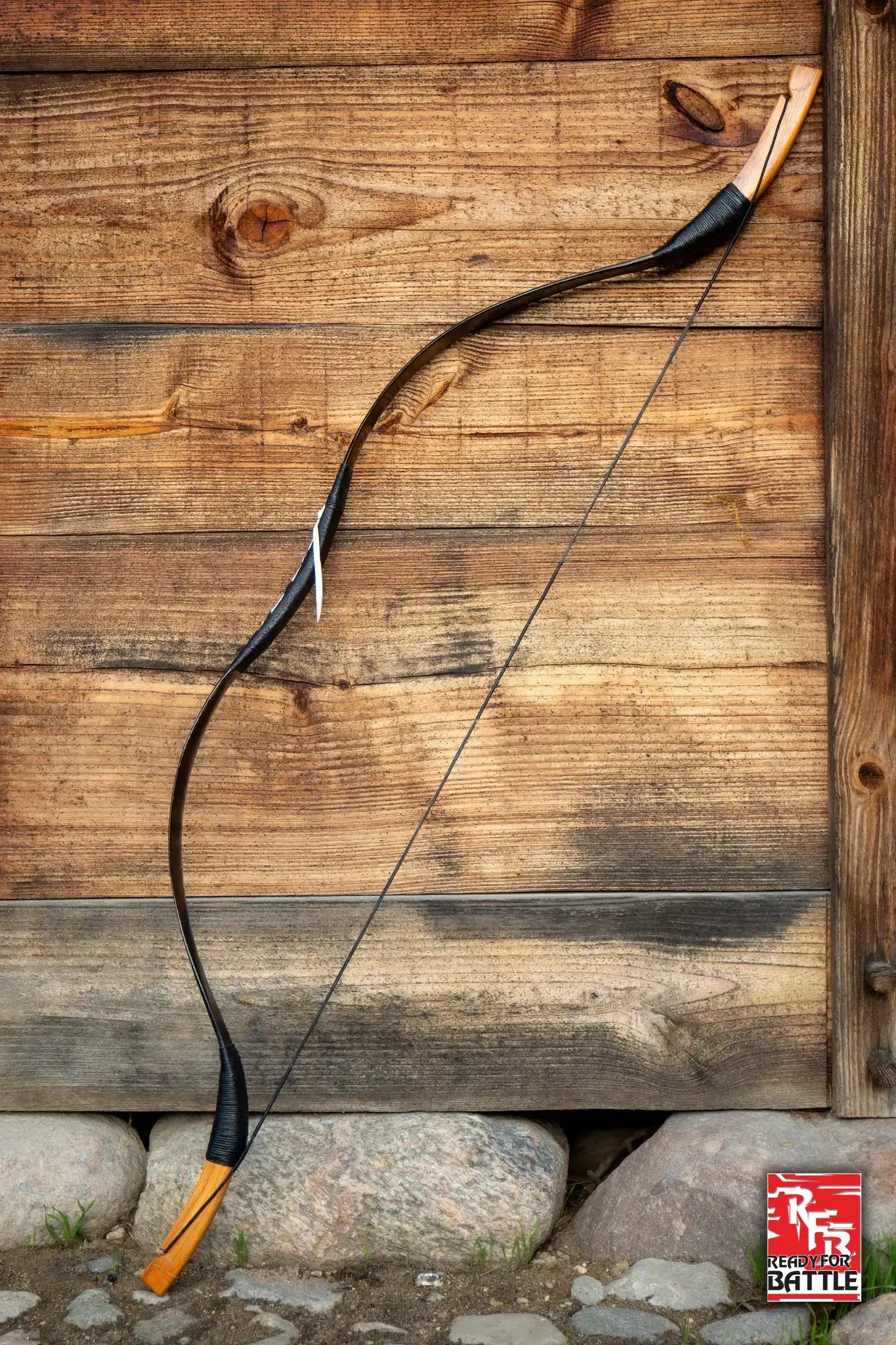 A traditional wooden bow hanging against a rustic wooden wall, part of the Bows collection at Epic Armoury.