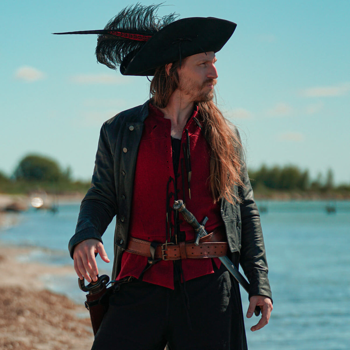 Man in a black pirate hat and leather jacket showcasing Mens Pirate Costumes by the water.