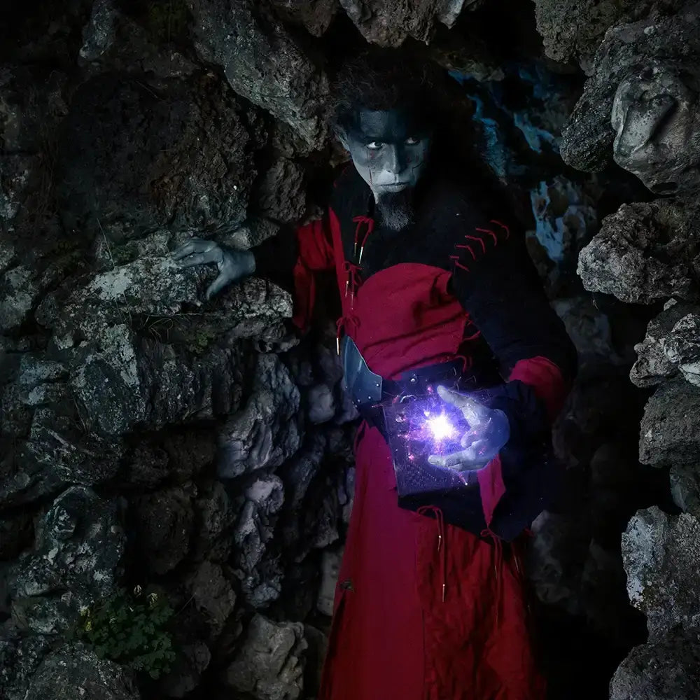 Mystical figure in a red robe casting magic in a dark rocky cave, showcasing intricate details and dramatic lighting.