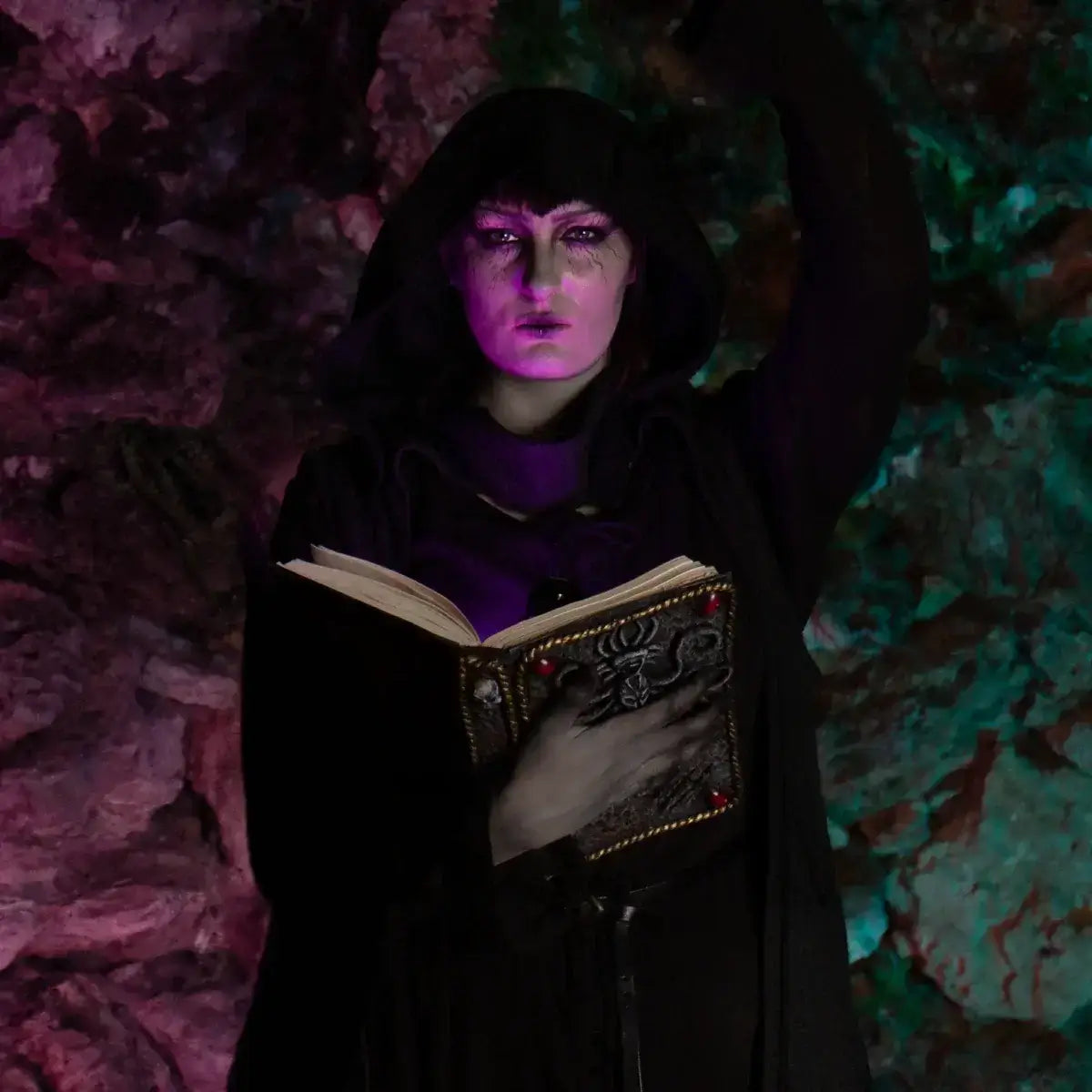 Mystical figure in a hooded cloak holding an ancient book, illuminated by colorful lights.