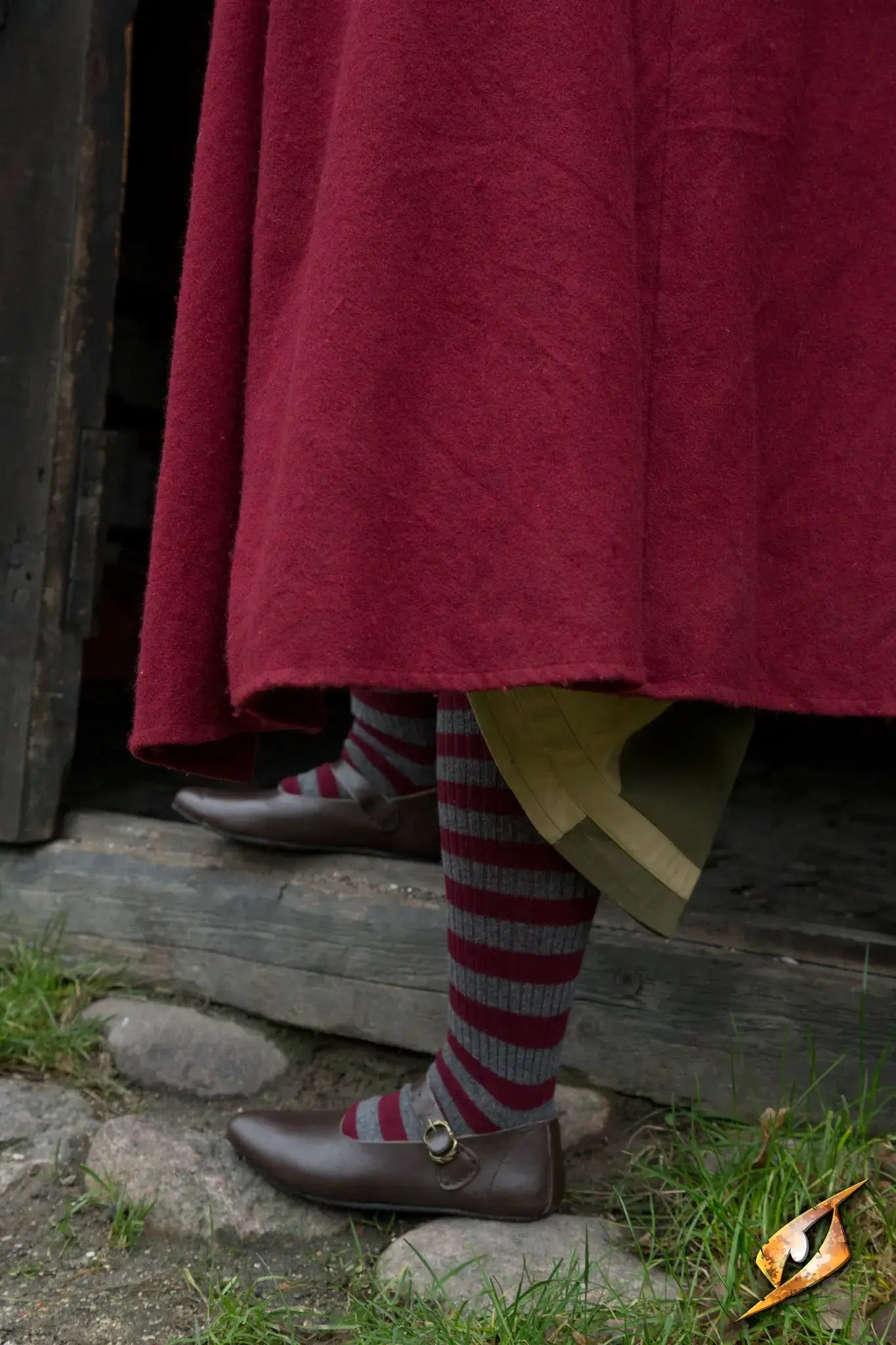 A close-up of Shoes Astrid on a person wearing striped socks and a long maroon garment.