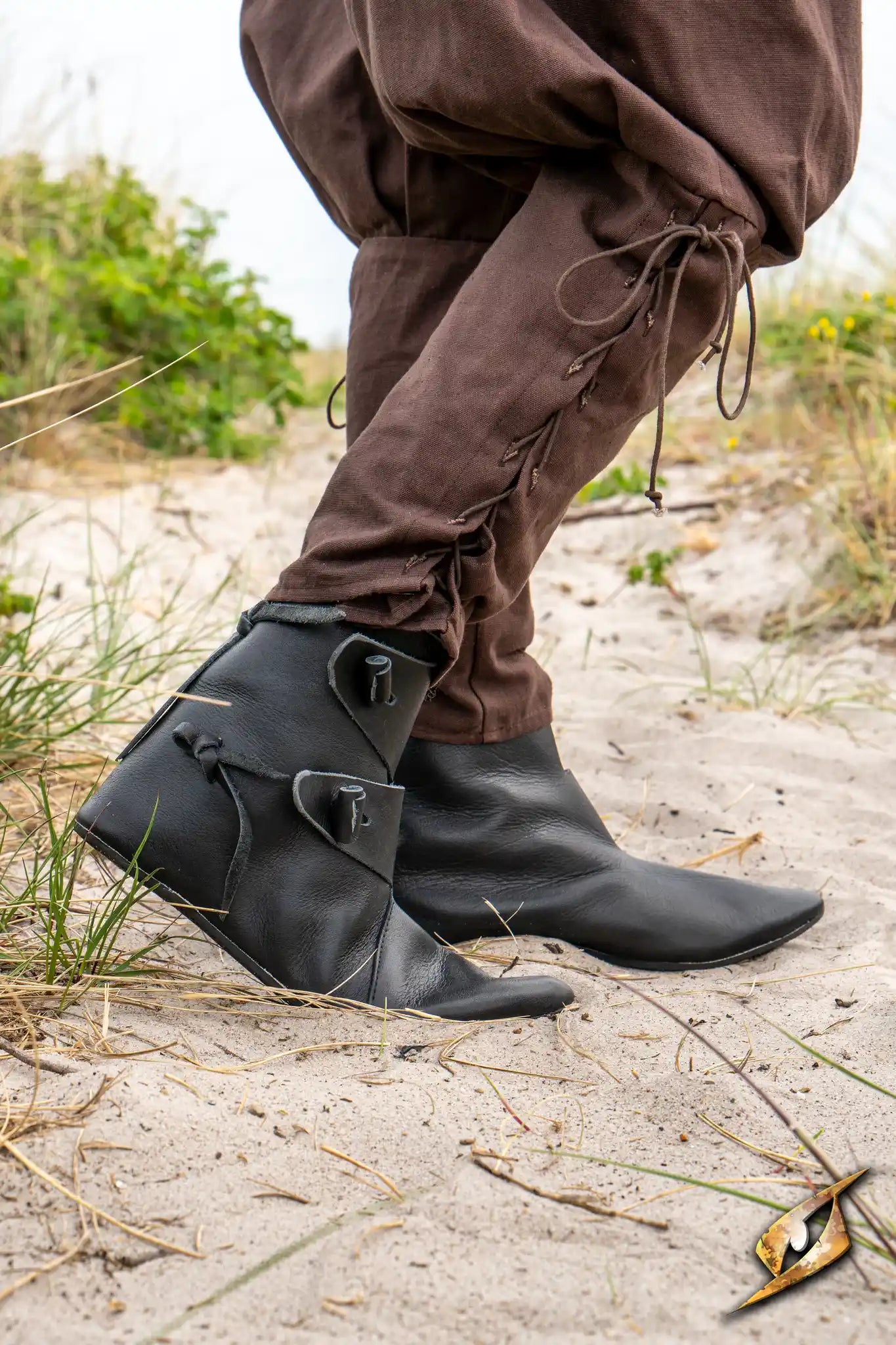 Shoes Jorik worn on feet in a sandy environment, featuring black leather design and medieval style.