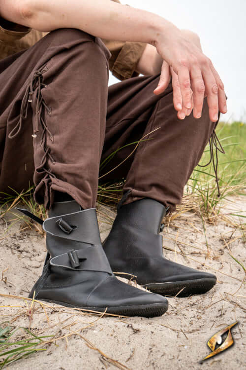 A close-up of Shoes Jorik, black leather Viking footwear, worn by a person sitting outdoors.
