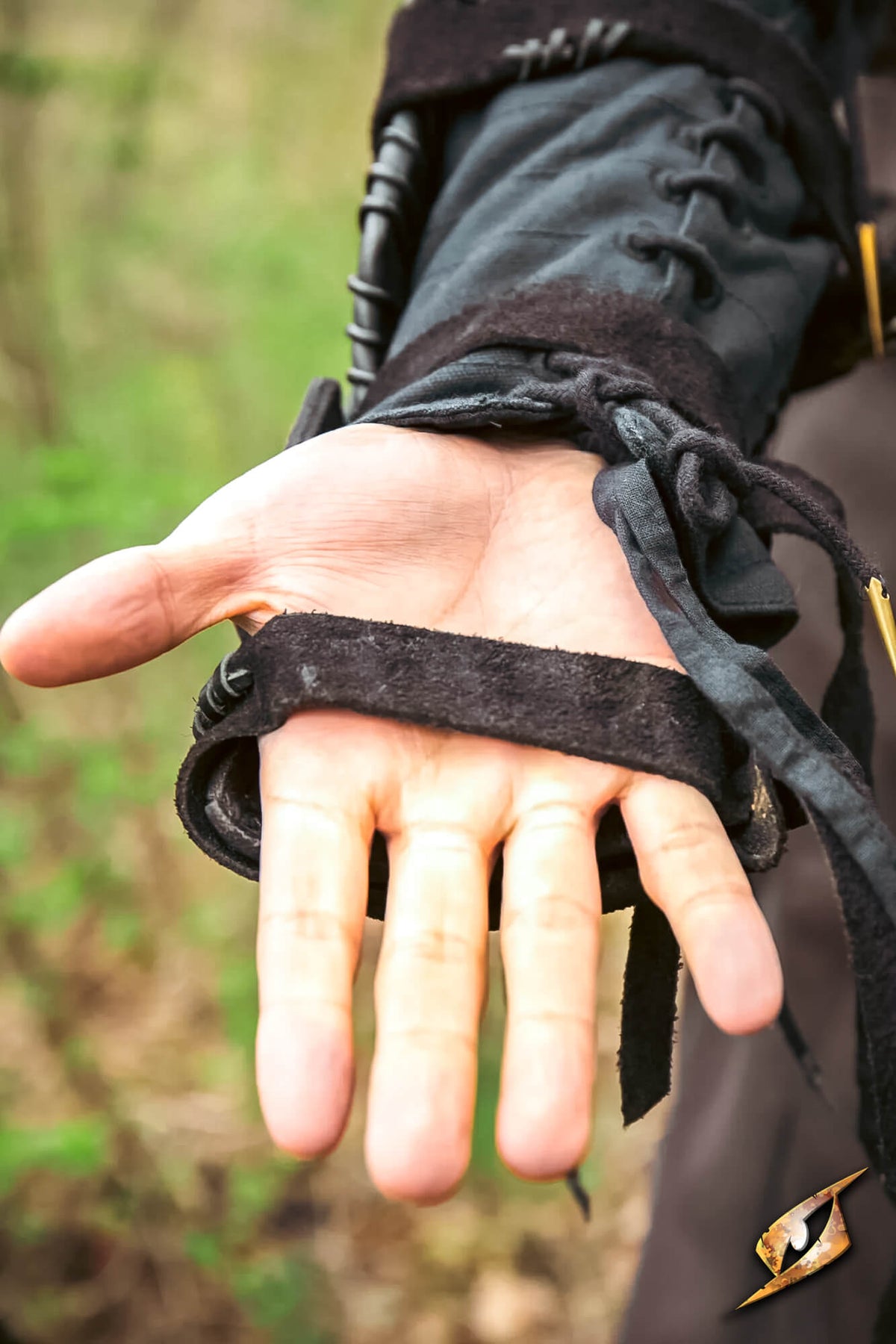 A close-up of a person's open hand wearing a black fingerless glove or wrist strap with lace-up cuffs, set against a blurred outdoor background.