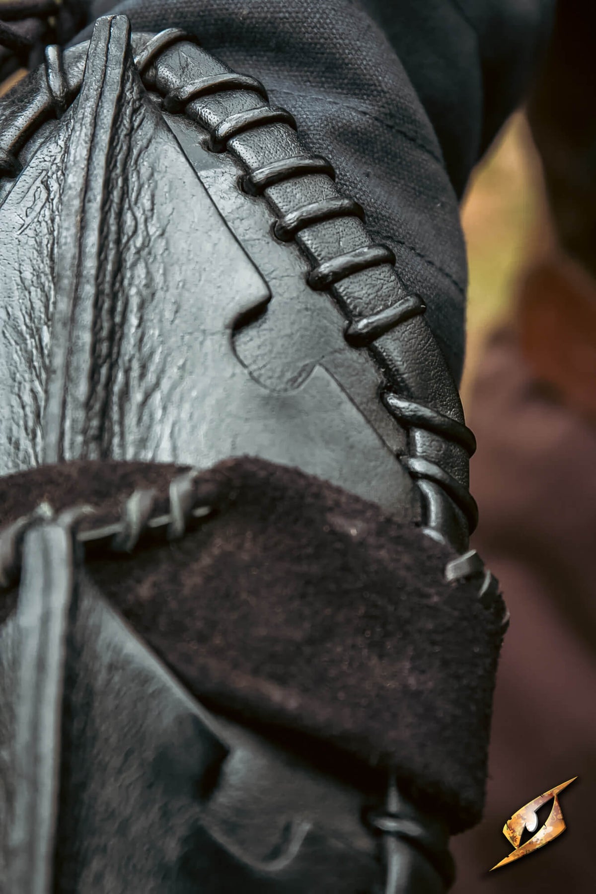 Close-up detail of a dark leather garment or accessory with decorative whipstitching and a dark brown suede-like trim, shown against a blurred warm-toned background.