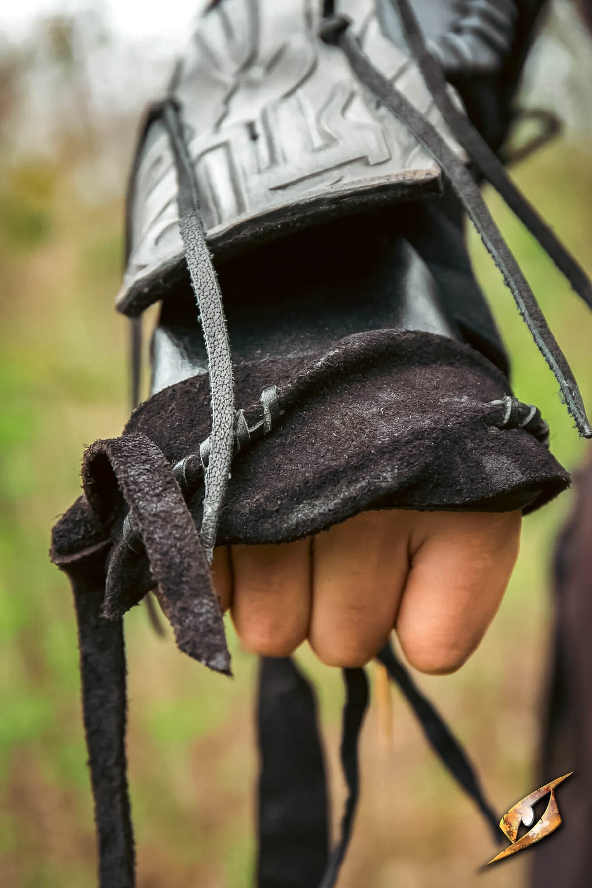 A close-up of a hand wearing a dark brown leather finger cleft glove with black laces, layered under a black leather gauntlet with a textured metal plate.