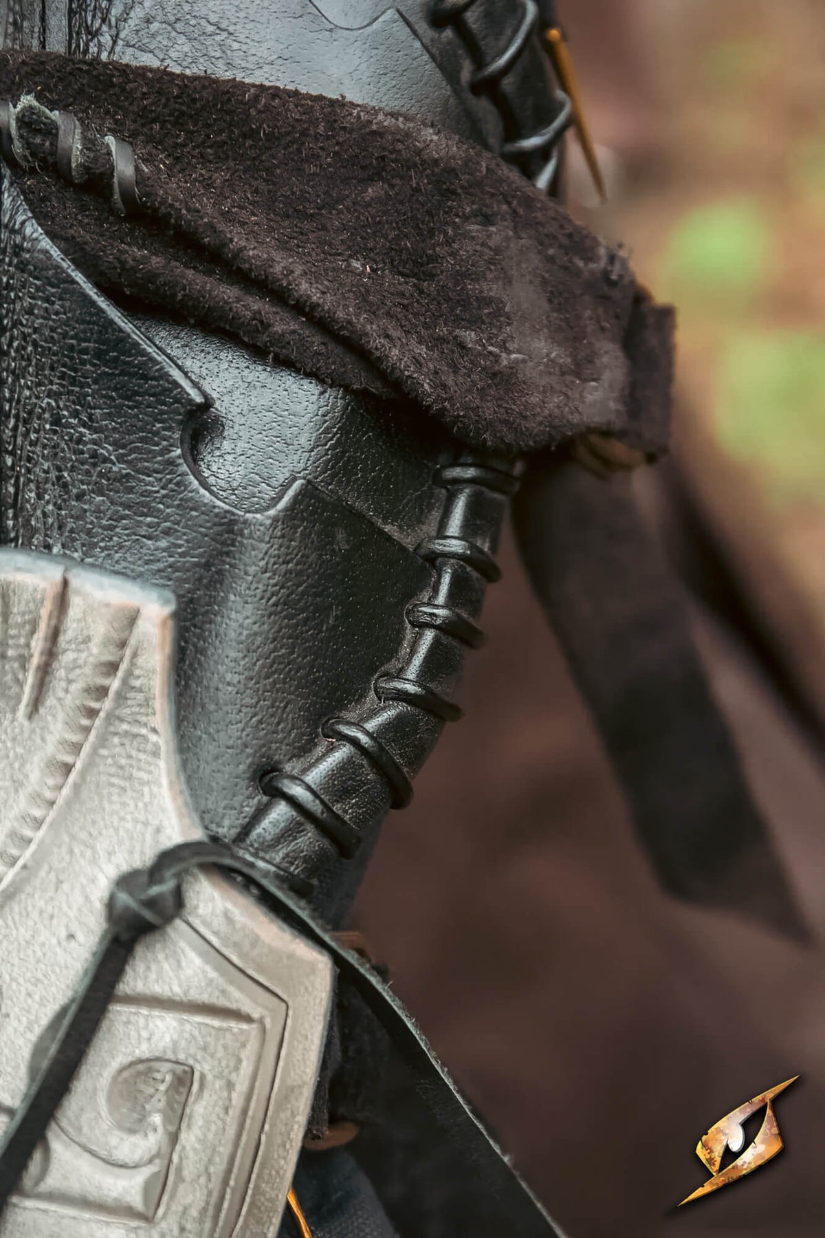 Close-up detail of a dark leather fantasy boot or armor piece with black laces, a brown fur trim, and a silver-toned metal plate, shown against a blurred brown background.