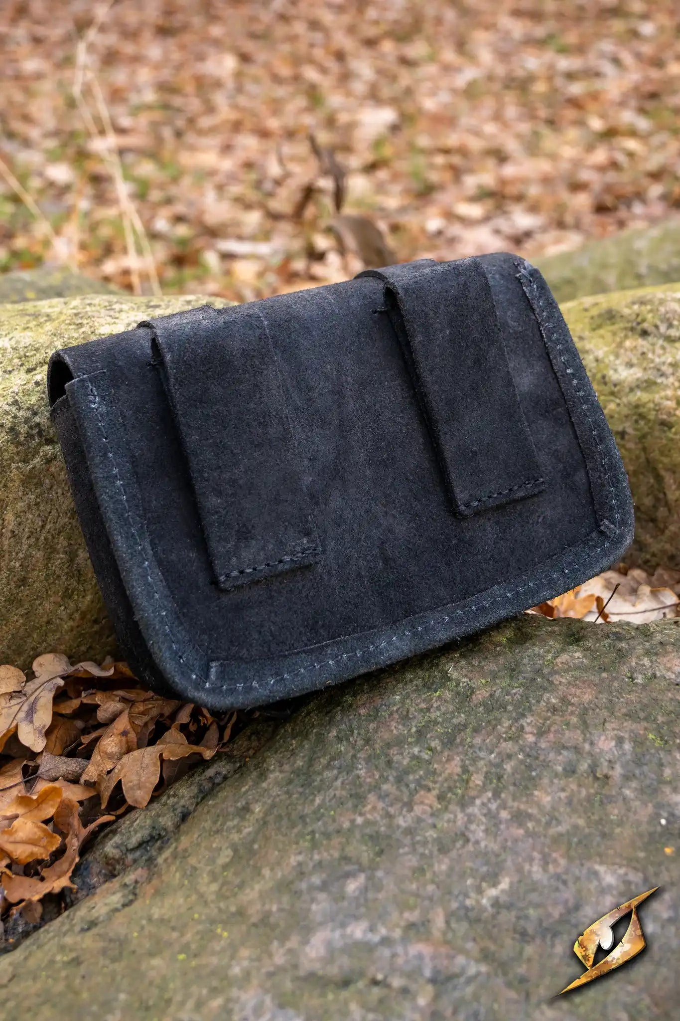Warrior bag - Suede - Large resting on a rock surrounded by fallen leaves in a natural setting.