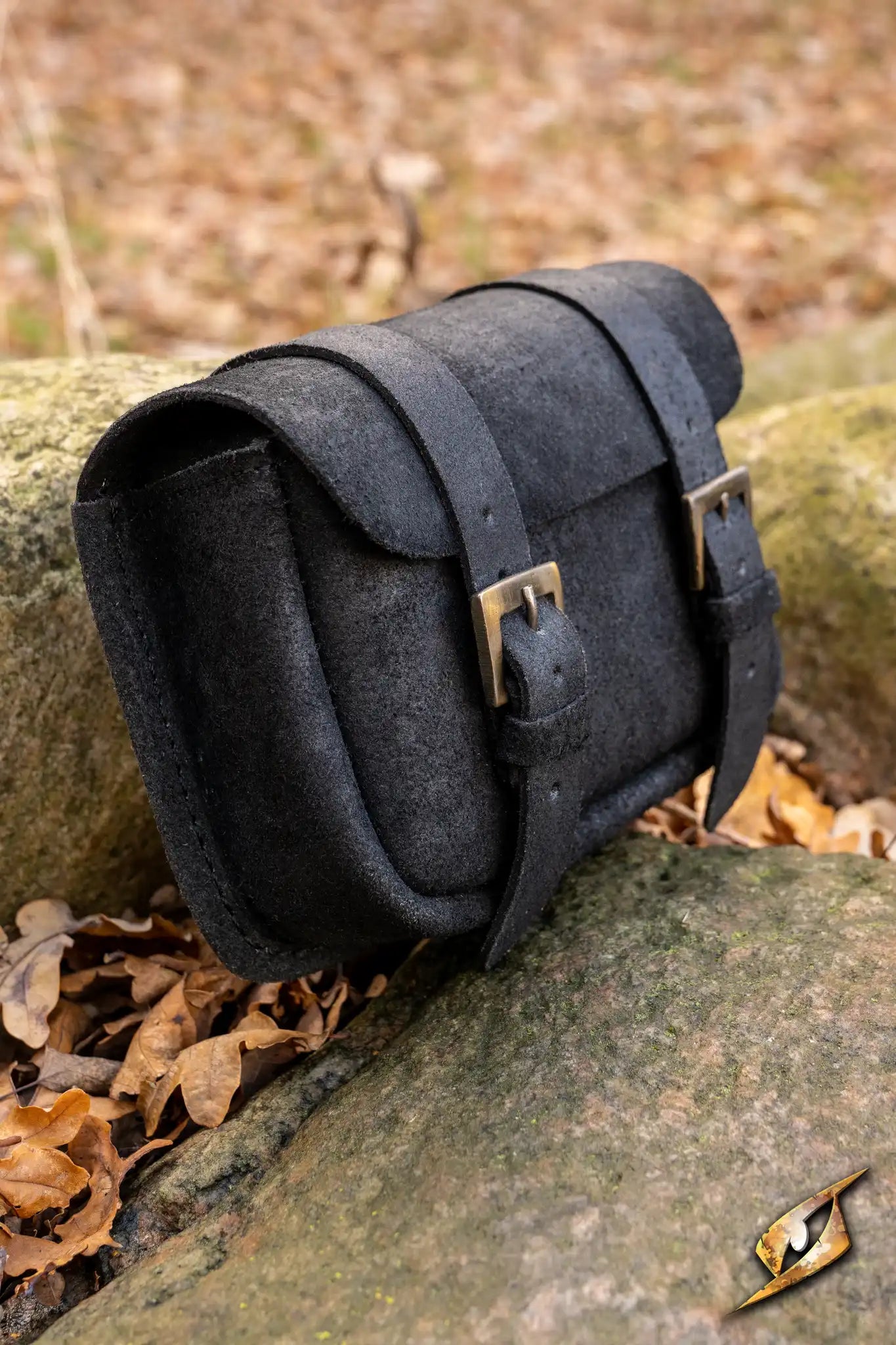 Warrior bag - Suede - Large placed on a rock among dried leaves, showcasing its stylish design and durability.