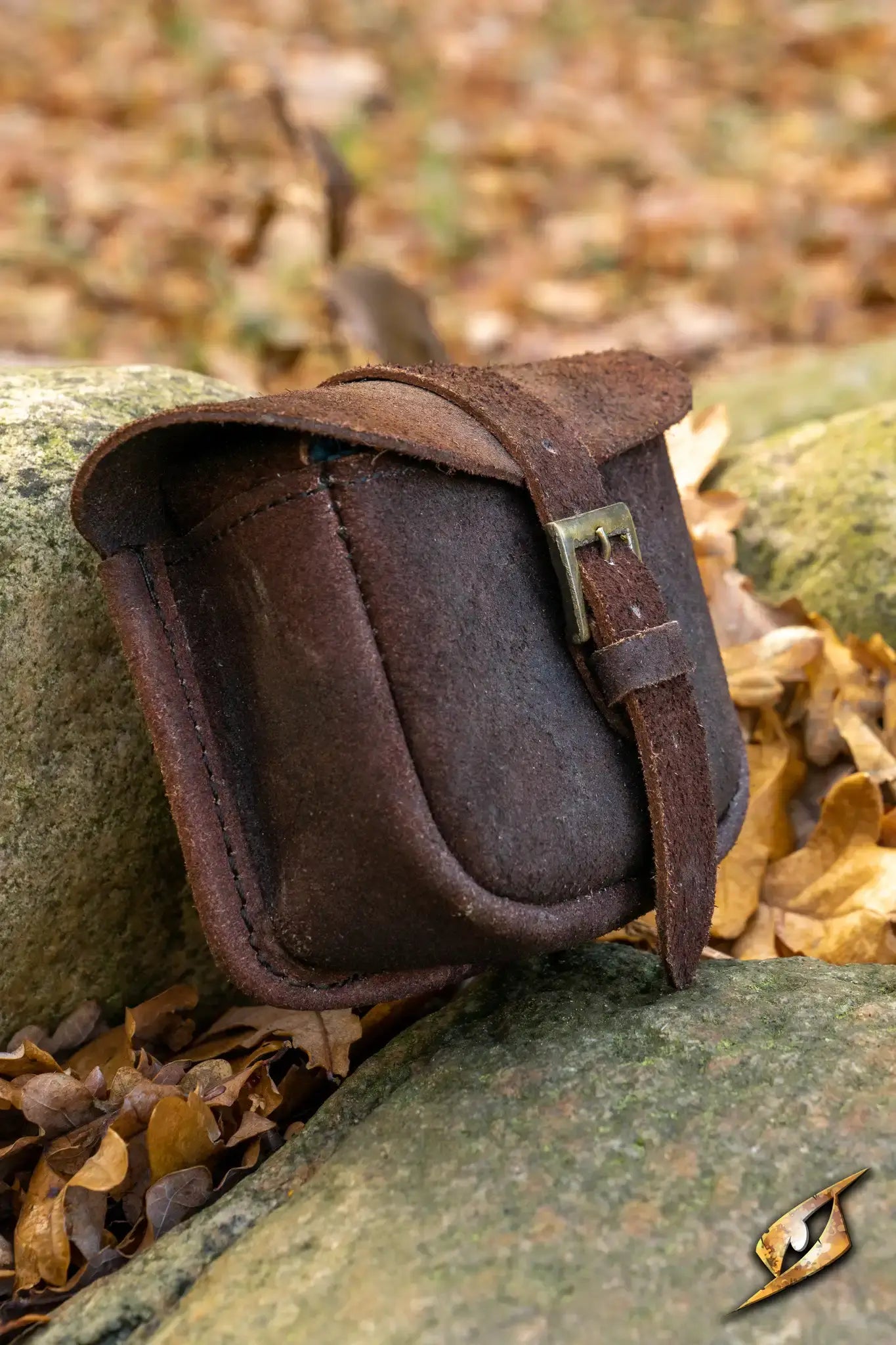 Warrior bag - Suede - Small resting on a rock surrounded by autumn leaves, showcasing its stylish design.