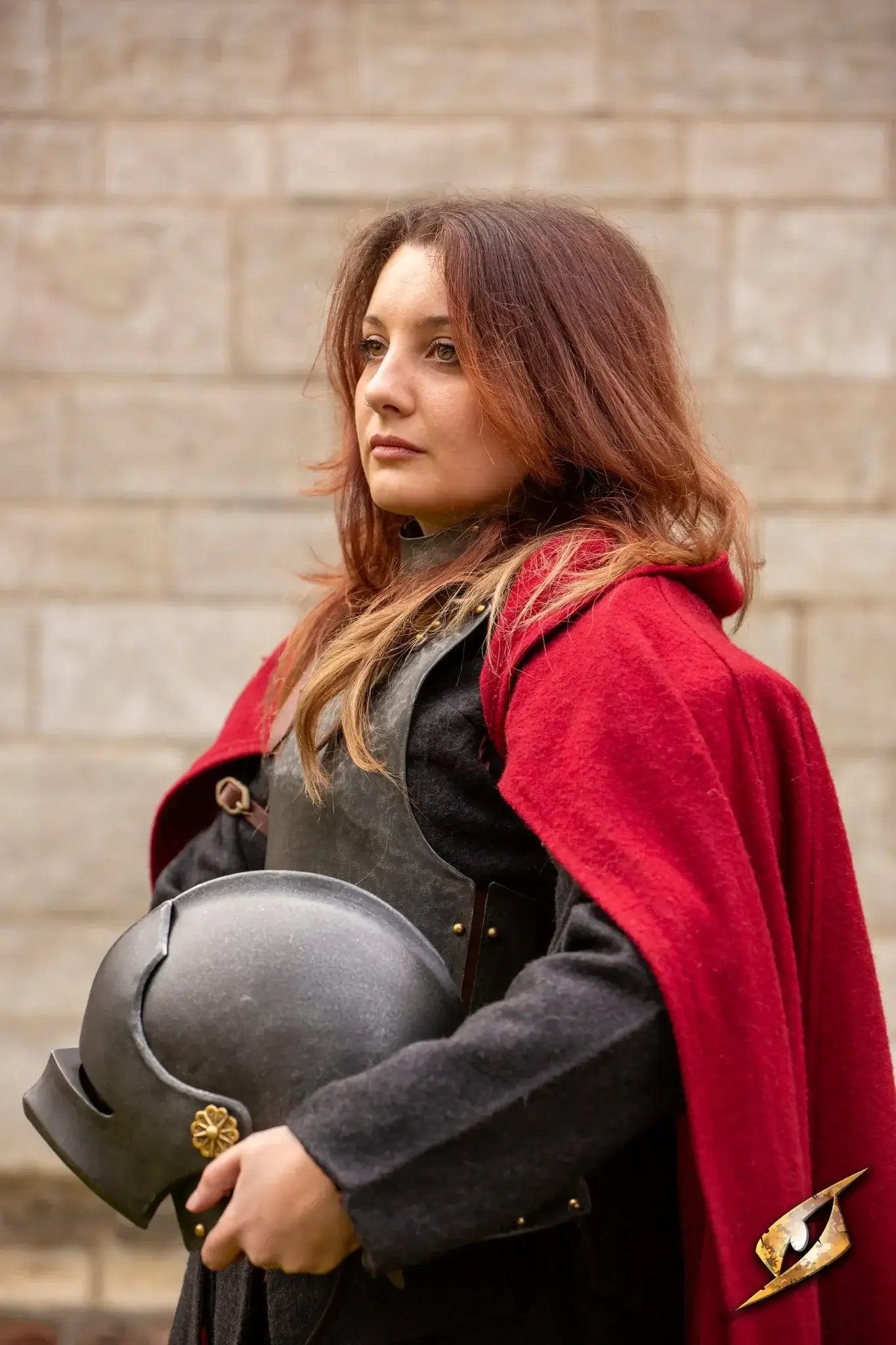 Renegade Helmet worn by a soldier in a red cloak, standing against a stone wall, representing military strength.