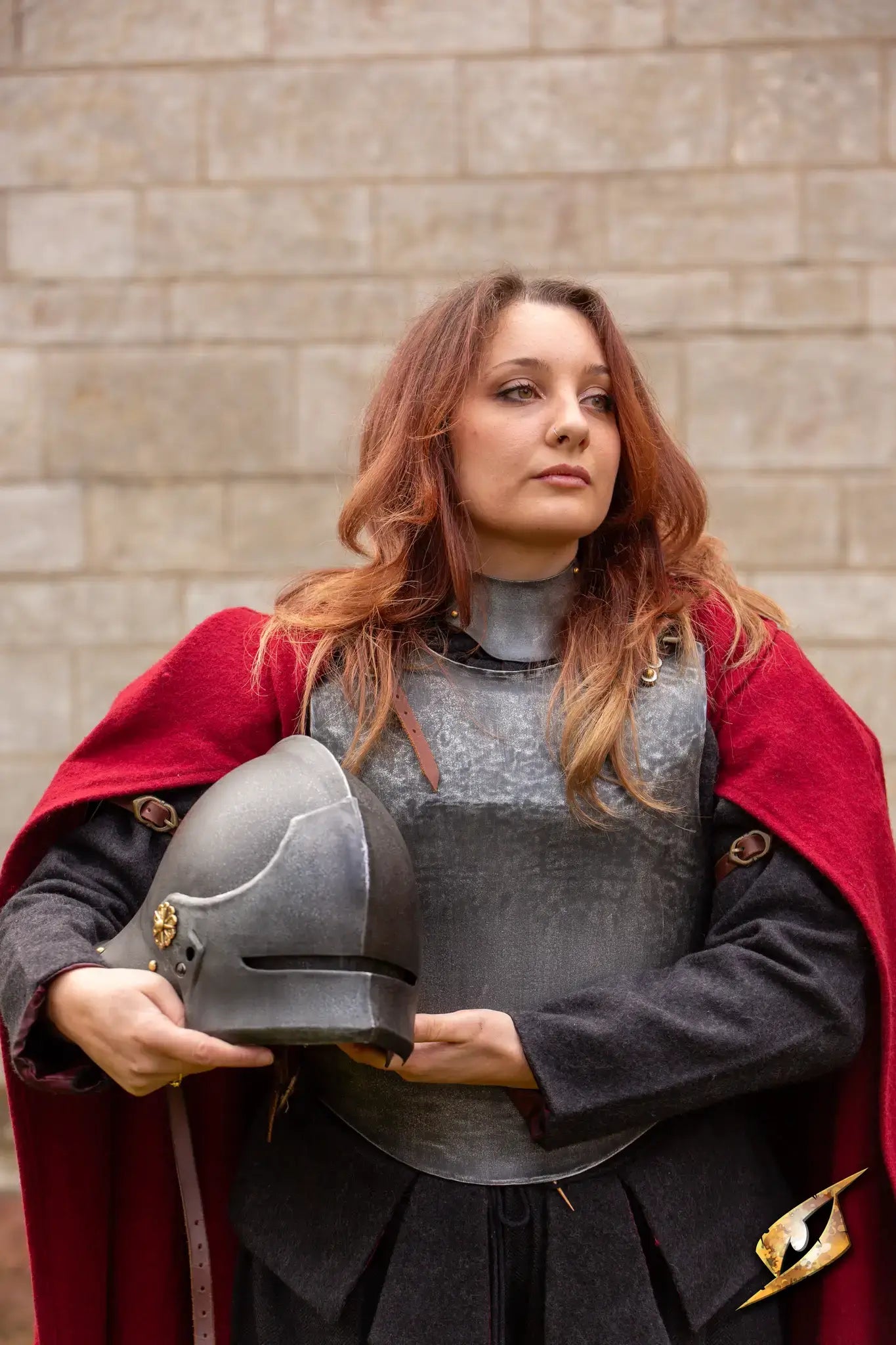 Woman in armor holding a Renegade Helmet, showcasing strength and confidence against a stone backdrop.