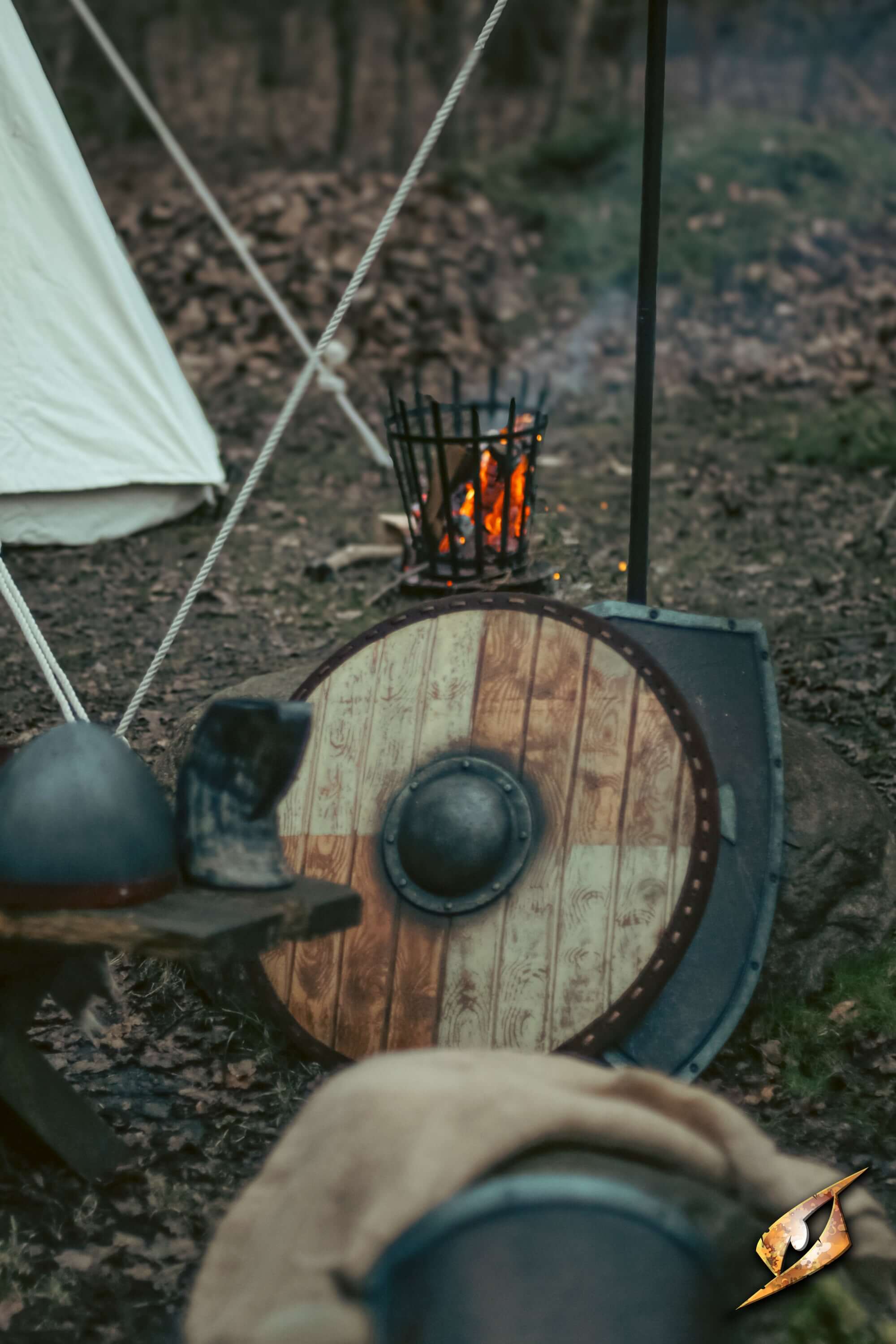 Thegn Shield leaning against a wooden table with a campfire burning in the background.