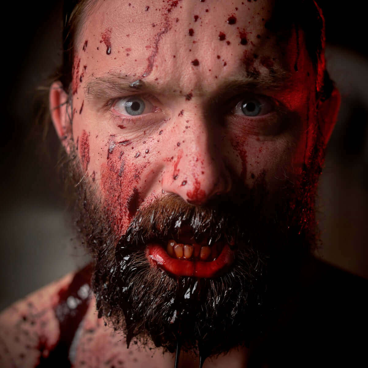 Intense close-up of a man with a blood-smeared face and a fierce expression, showcasing dramatic lighting and details.