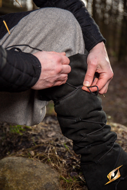 Person adjusting Theoderic gaiters while standing on a forest trail.