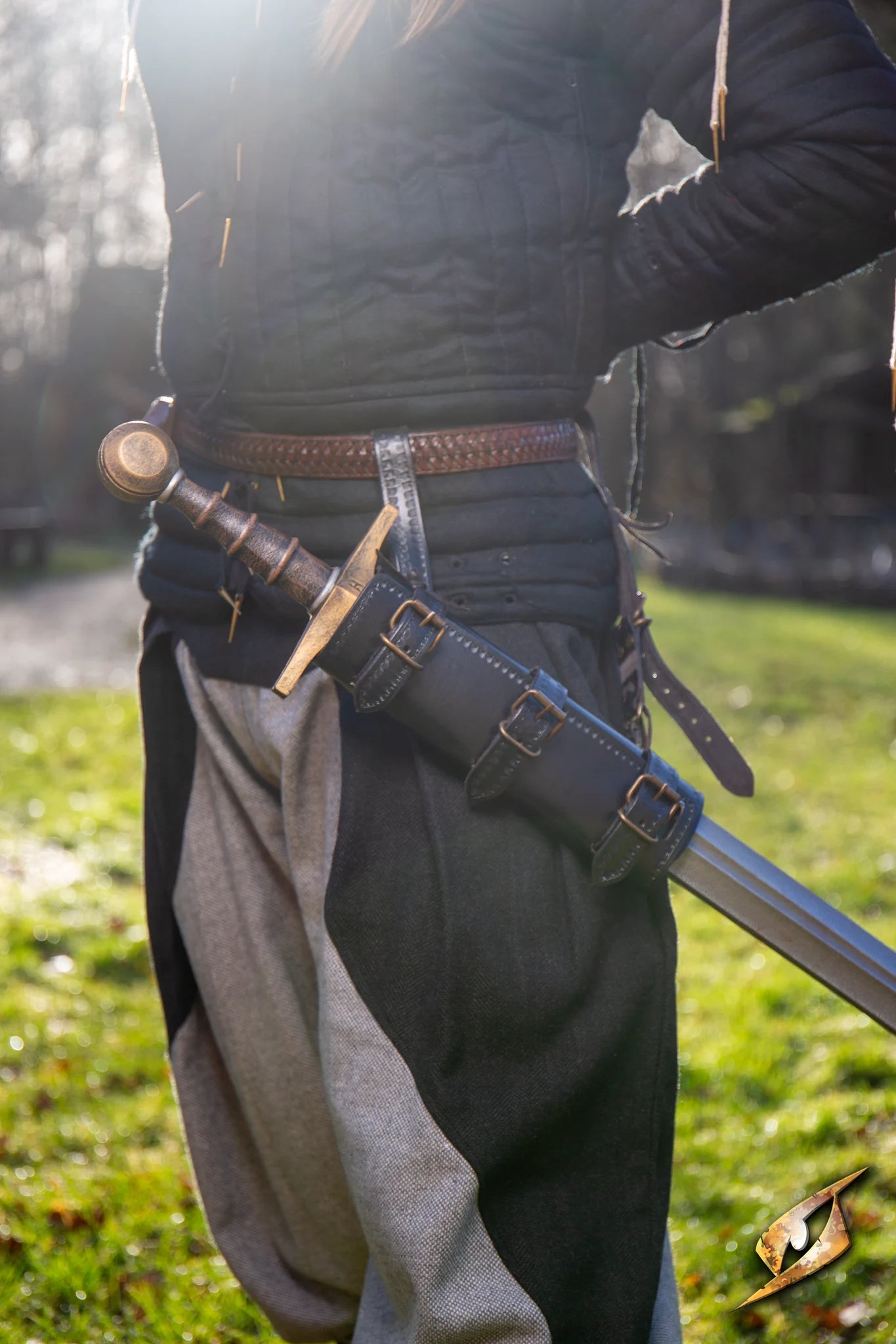 A person wearing a belt with an Adjustable Scabbard holding a sword, outdoors in a sunny environment.