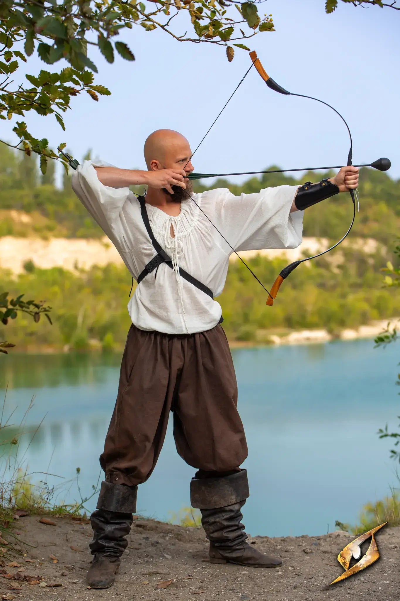 Man in historical outfit demonstrating archery technique while wearing an Archery Bracer by a serene lake.