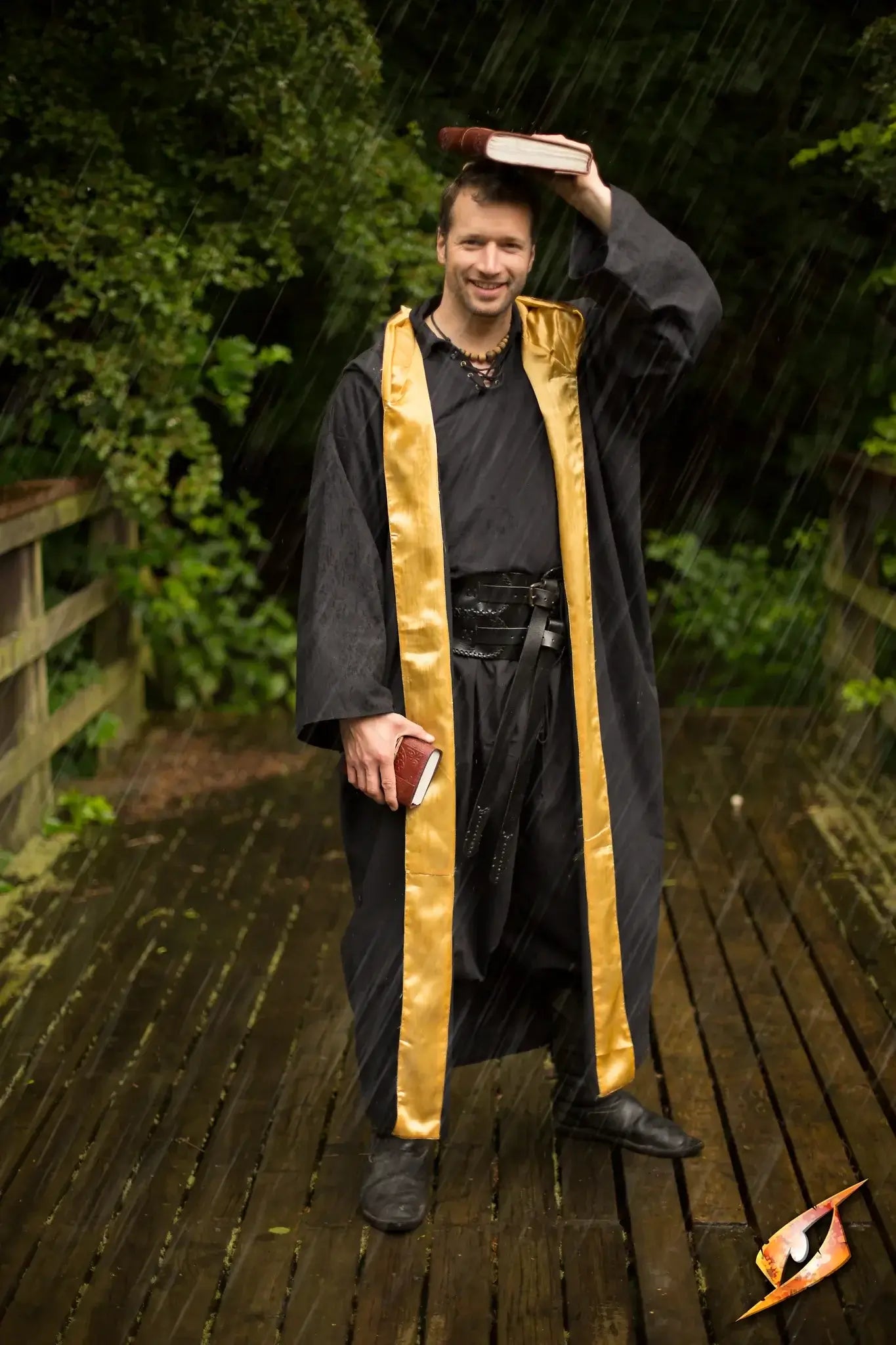 A magician wearing a black Magician Robe with gold trim, holding books outdoors in the rain.