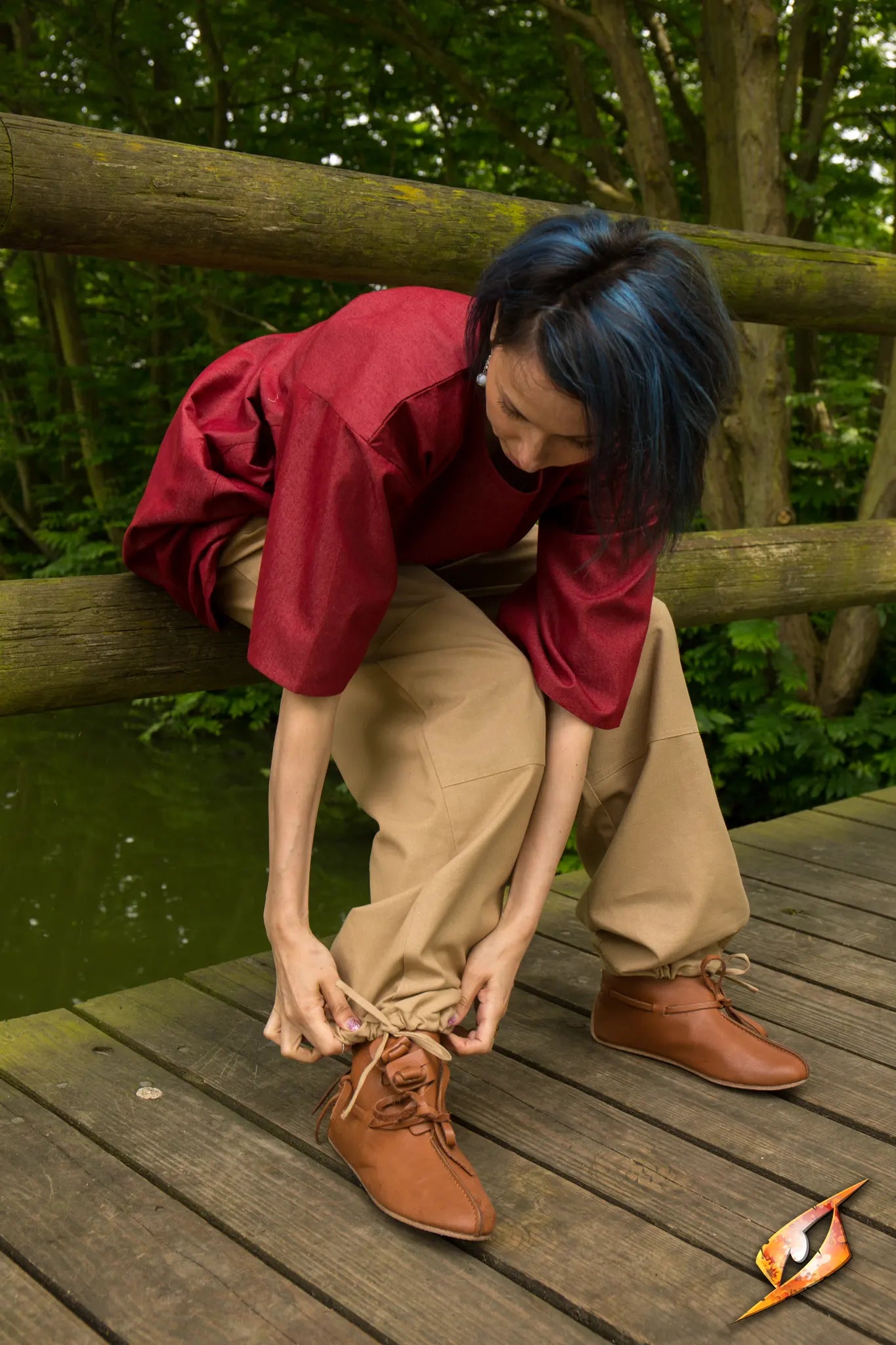 Person tying shoelaces while wearing Basic Pants on a wooden bridge in a lush green setting.