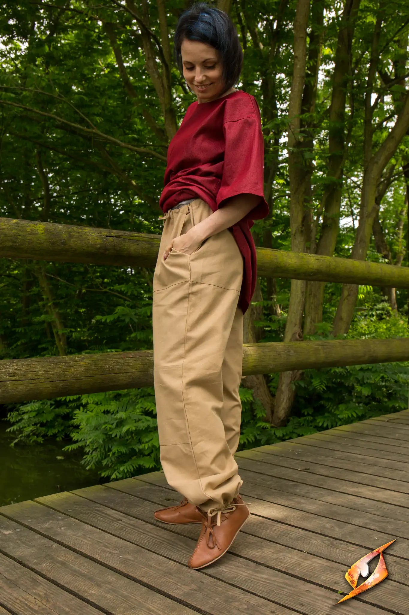Woman standing in Basic Pants on a wooden bridge surrounded by green trees.