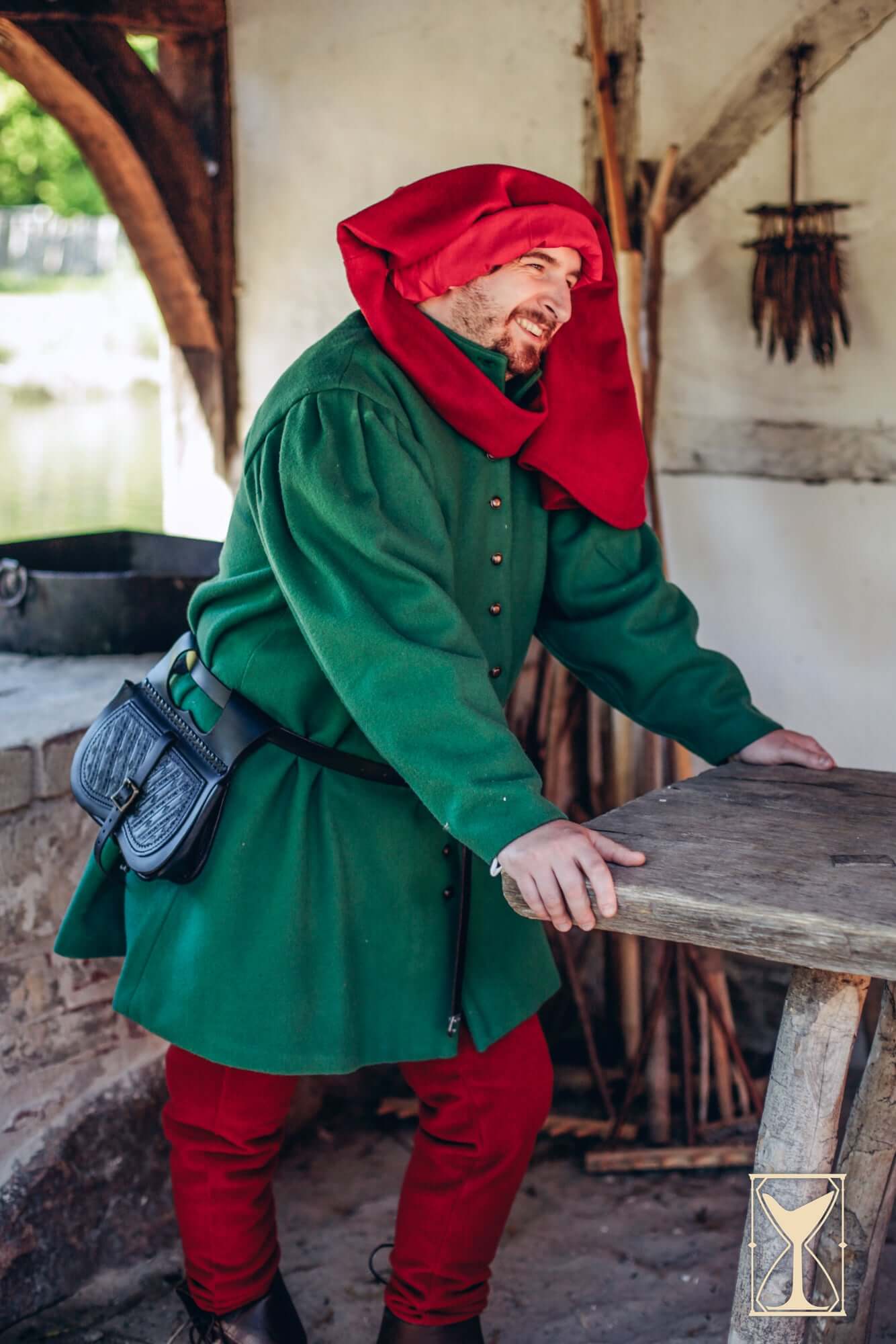 Man in historical green Surcoat Lorenzo with red hood, showcasing 14th century styled attire.