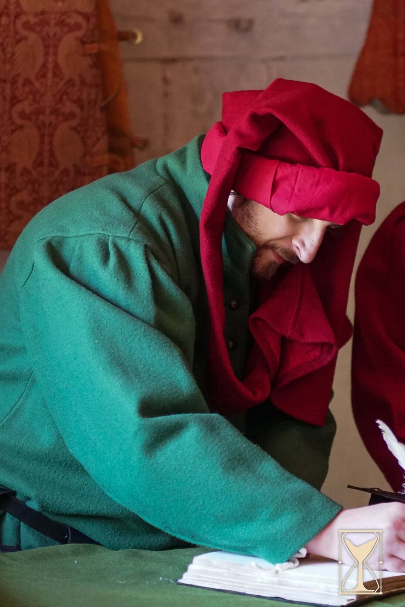 A man in a green surcoat with a red hood, writing, reflecting 14th century fashion, reminiscent of the Surcoat Lorenzo style.