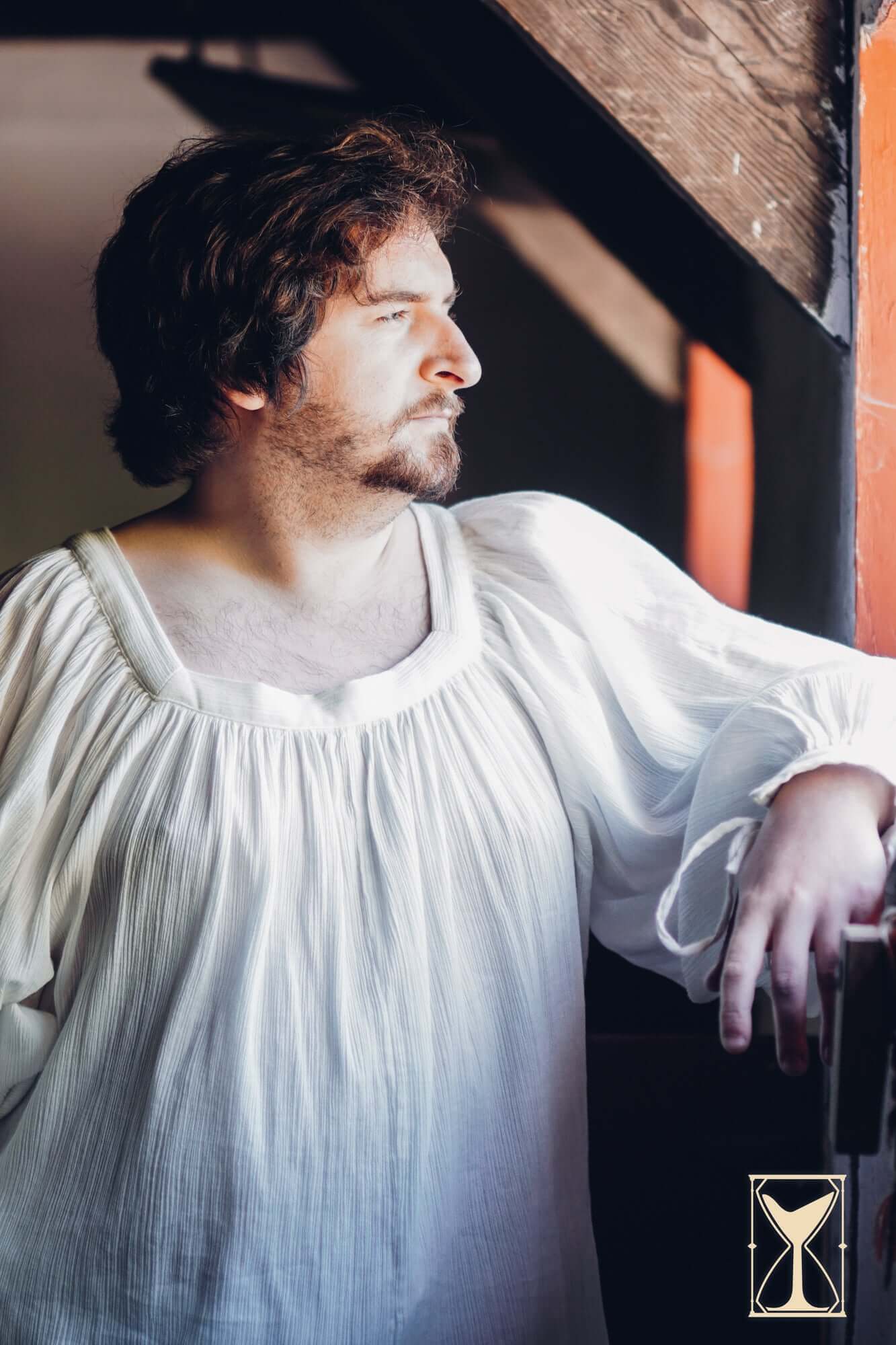 Shirt Duccio model standing by a window, showcasing a medieval-style shirt with relaxed fit and soft fabric.