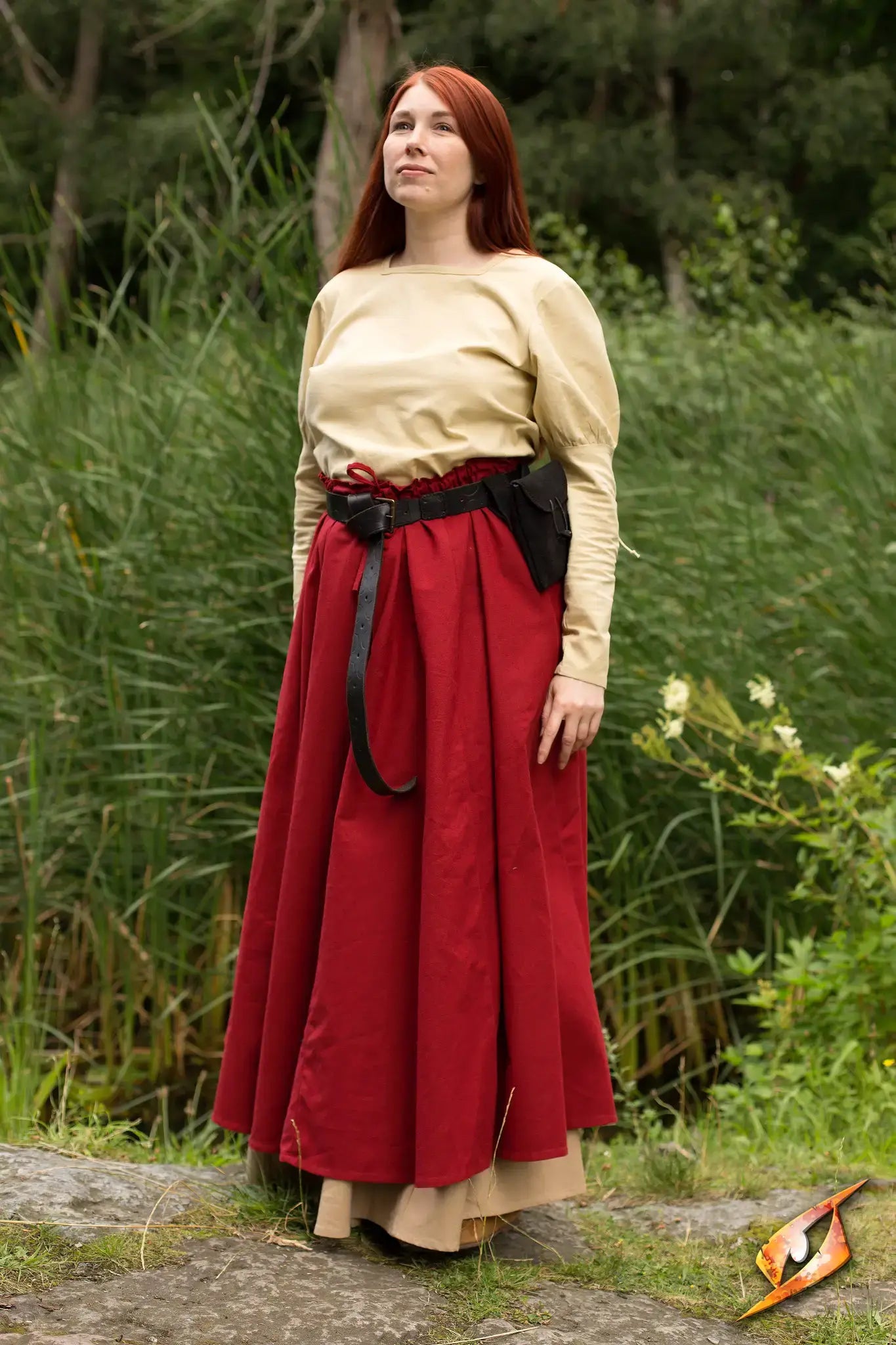 A woman wearing a stylish Empire Shirt with puffy shoulders and a long red skirt, posing near greenery.