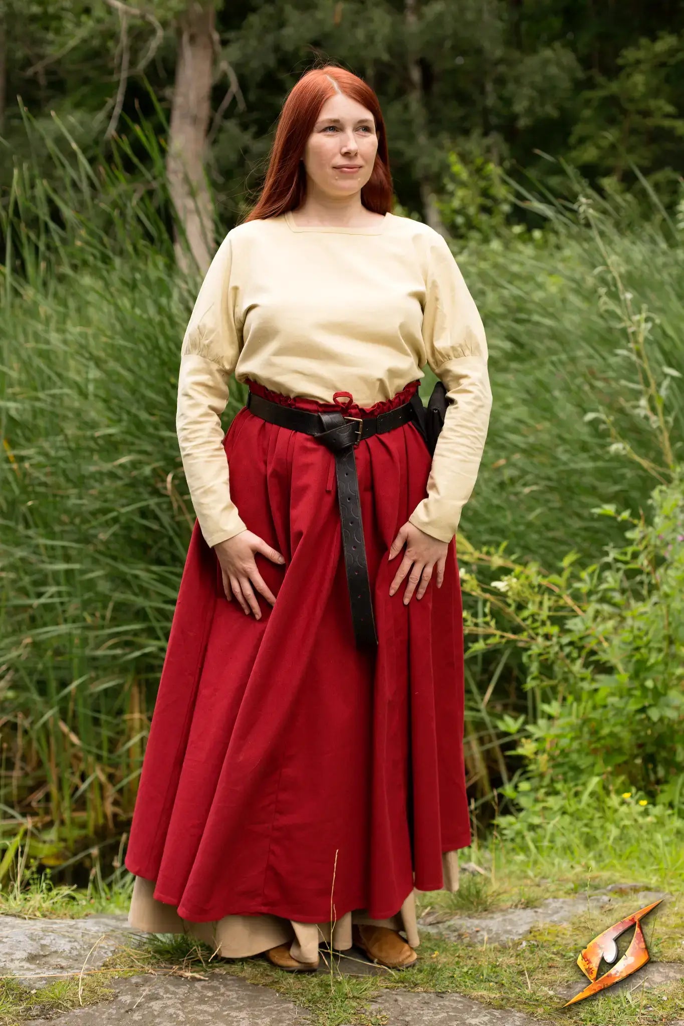 Woman wearing an Empire Shirt with puffy shoulders and a red skirt in a natural setting.