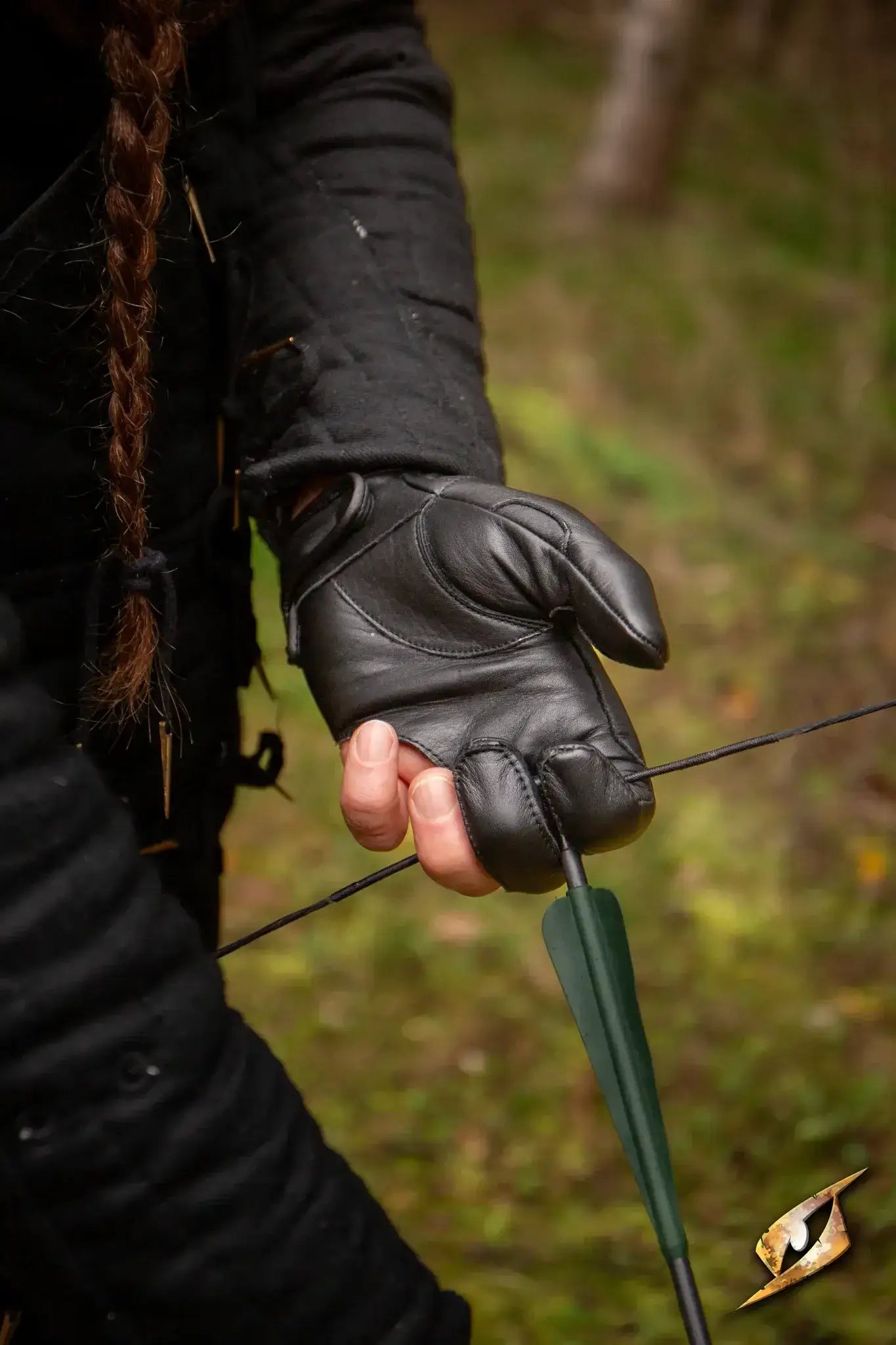 Archery Half-glove worn by an archer gripping a bowstring in a forest setting.