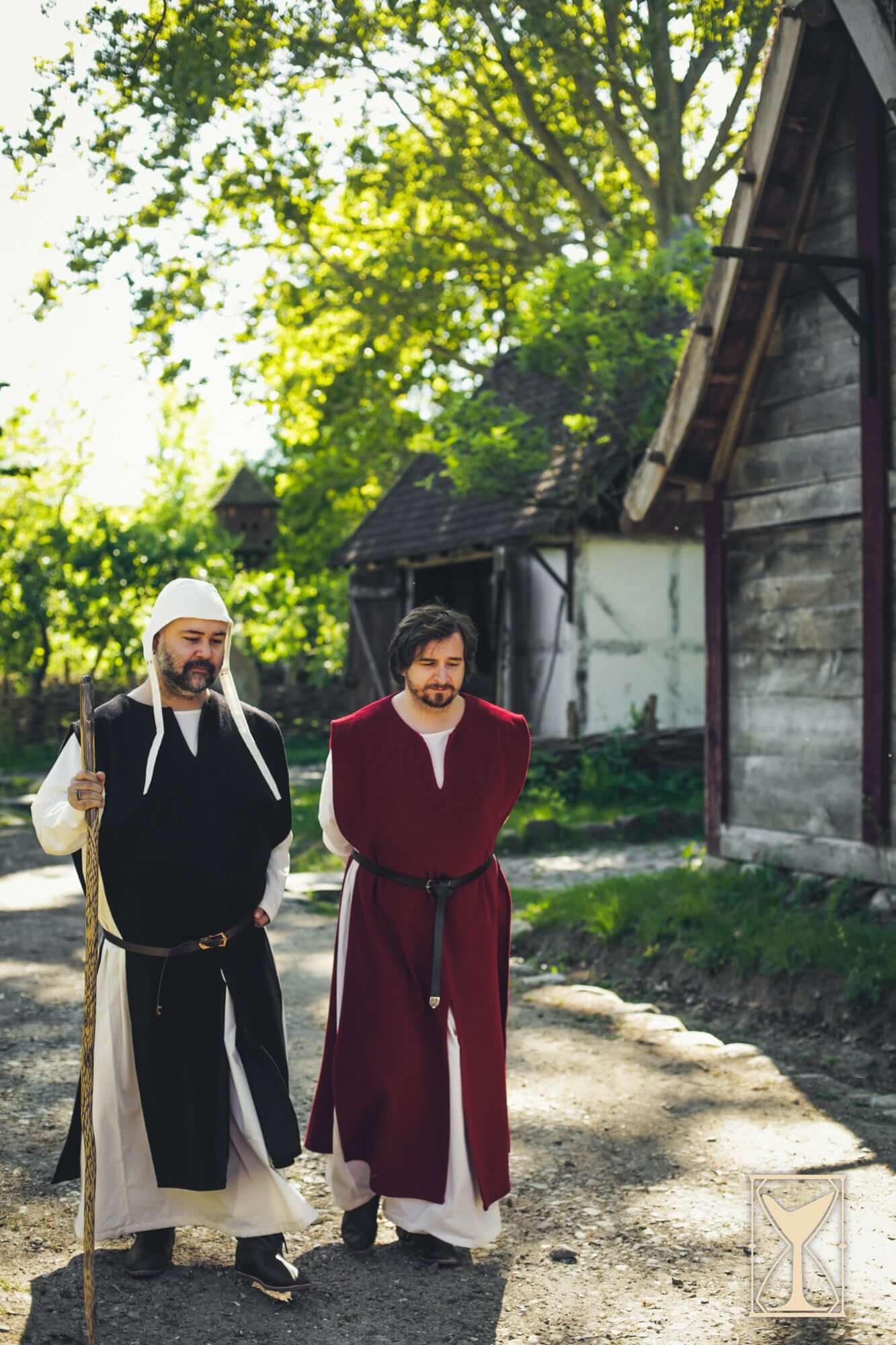 Two men wearing Cyclas Bernard over-tunics walking in a medieval setting, showcasing layered historical attire.