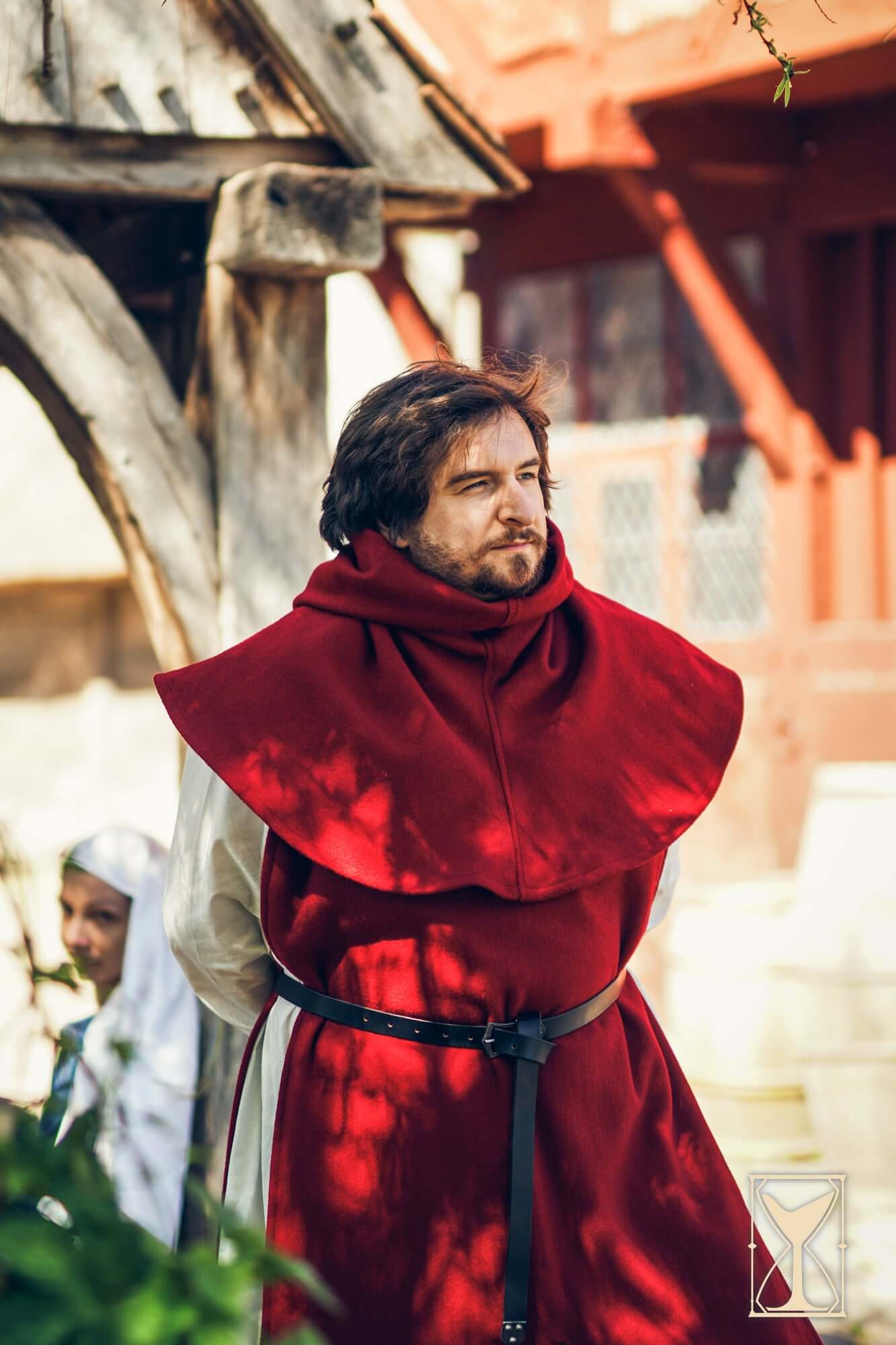 Man wearing a red Cyclas Bernard over-tunic, showcasing medieval fashion grounded in historical realism.