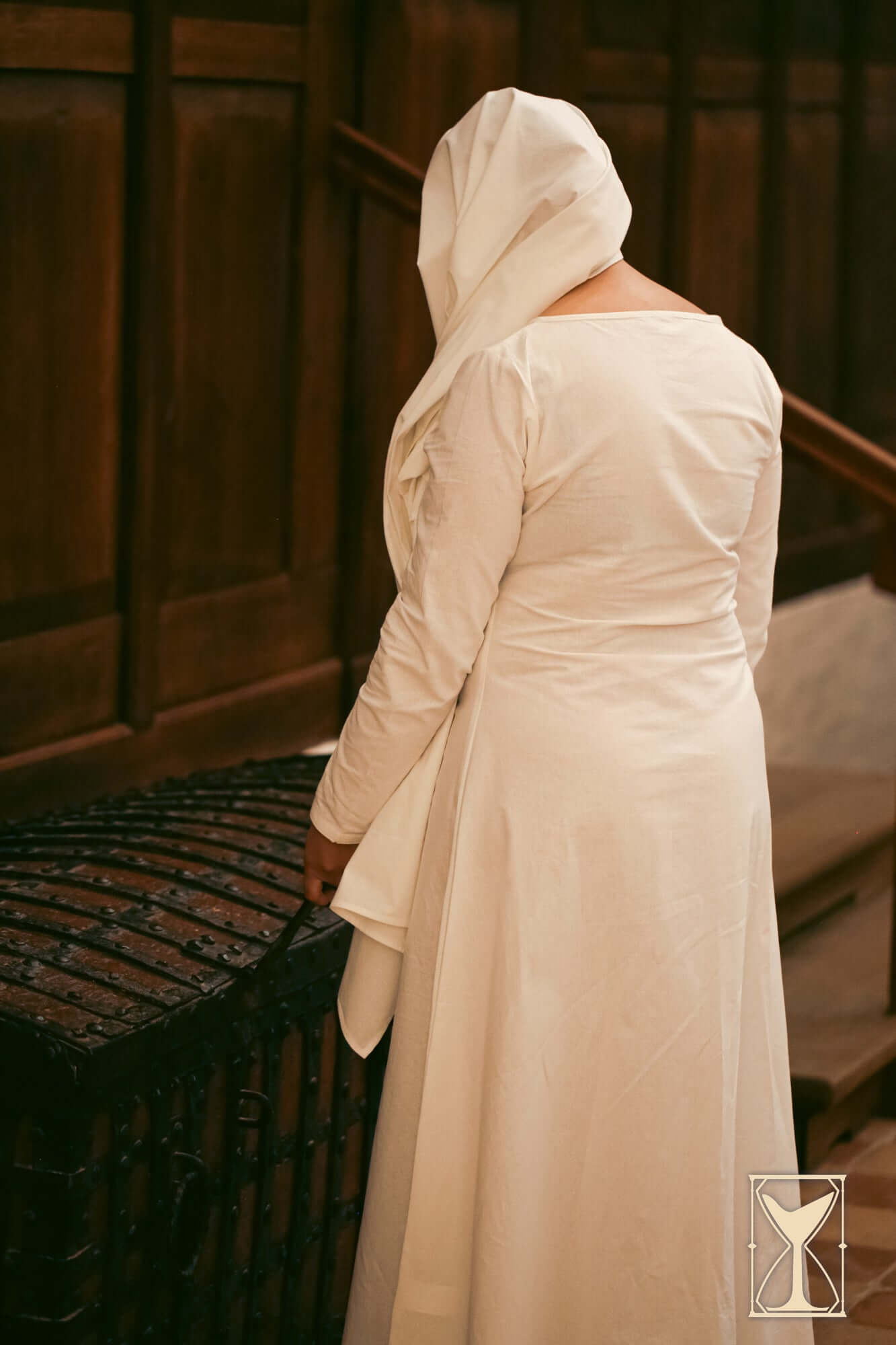 Back view of a woman wearing a medieval Chemise with a hood, showcasing soft fabric against a wooden backdrop.
