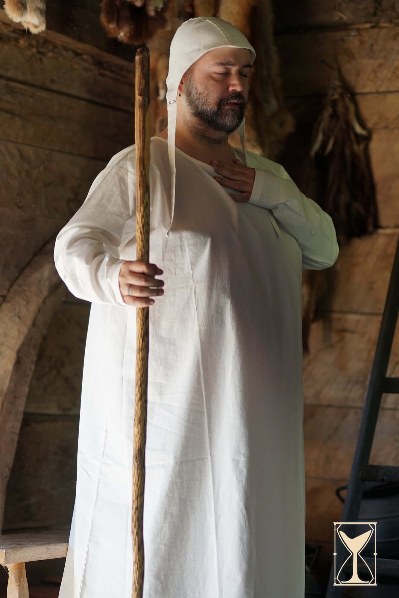 Man wearing the Undertunic Modesto, standing with a staff in a medieval setting, embodying historical accuracy.