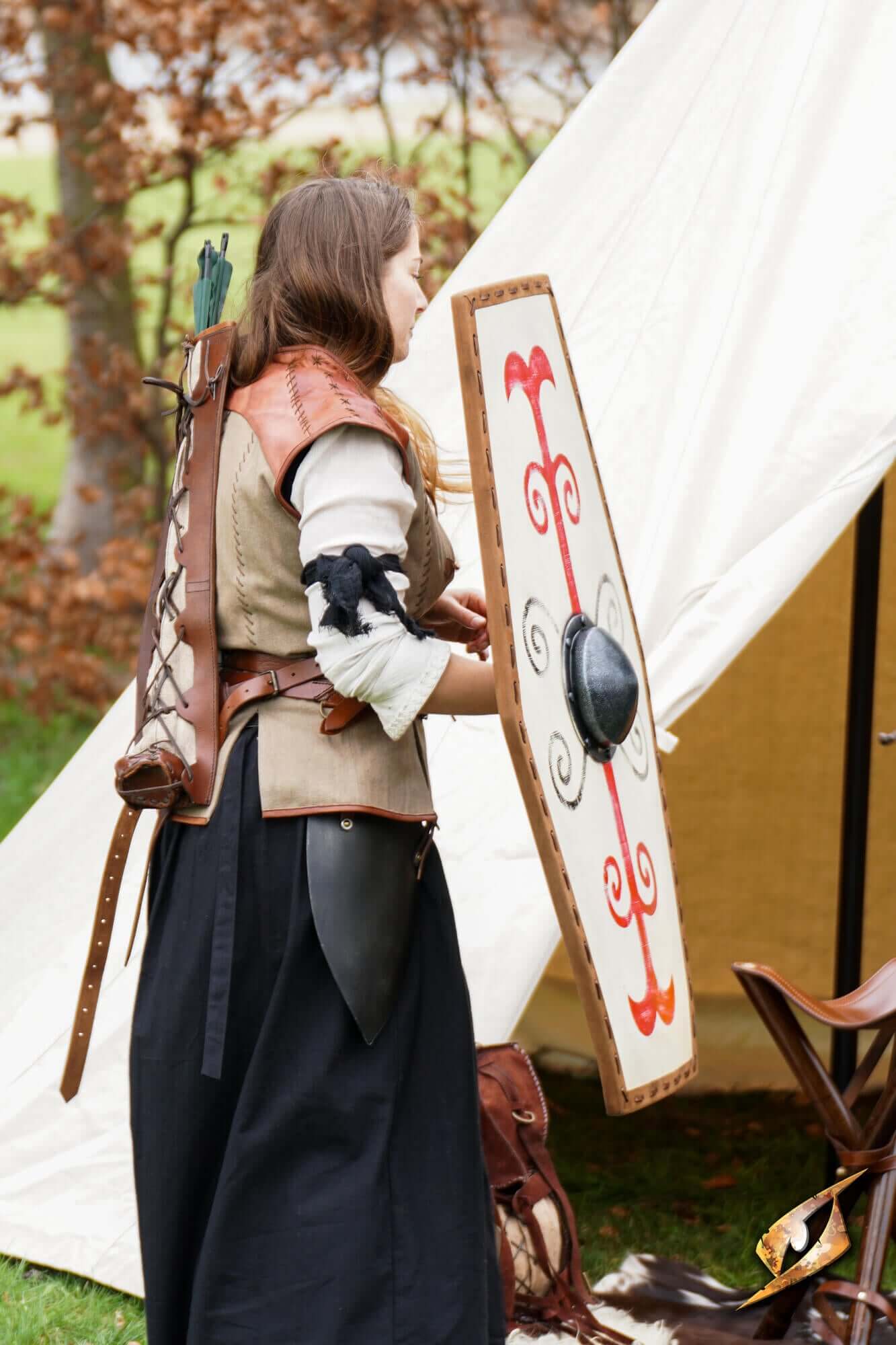 A warrior holding a Germanic Shield decorated with red tribal markings, ready for battle outdoors.