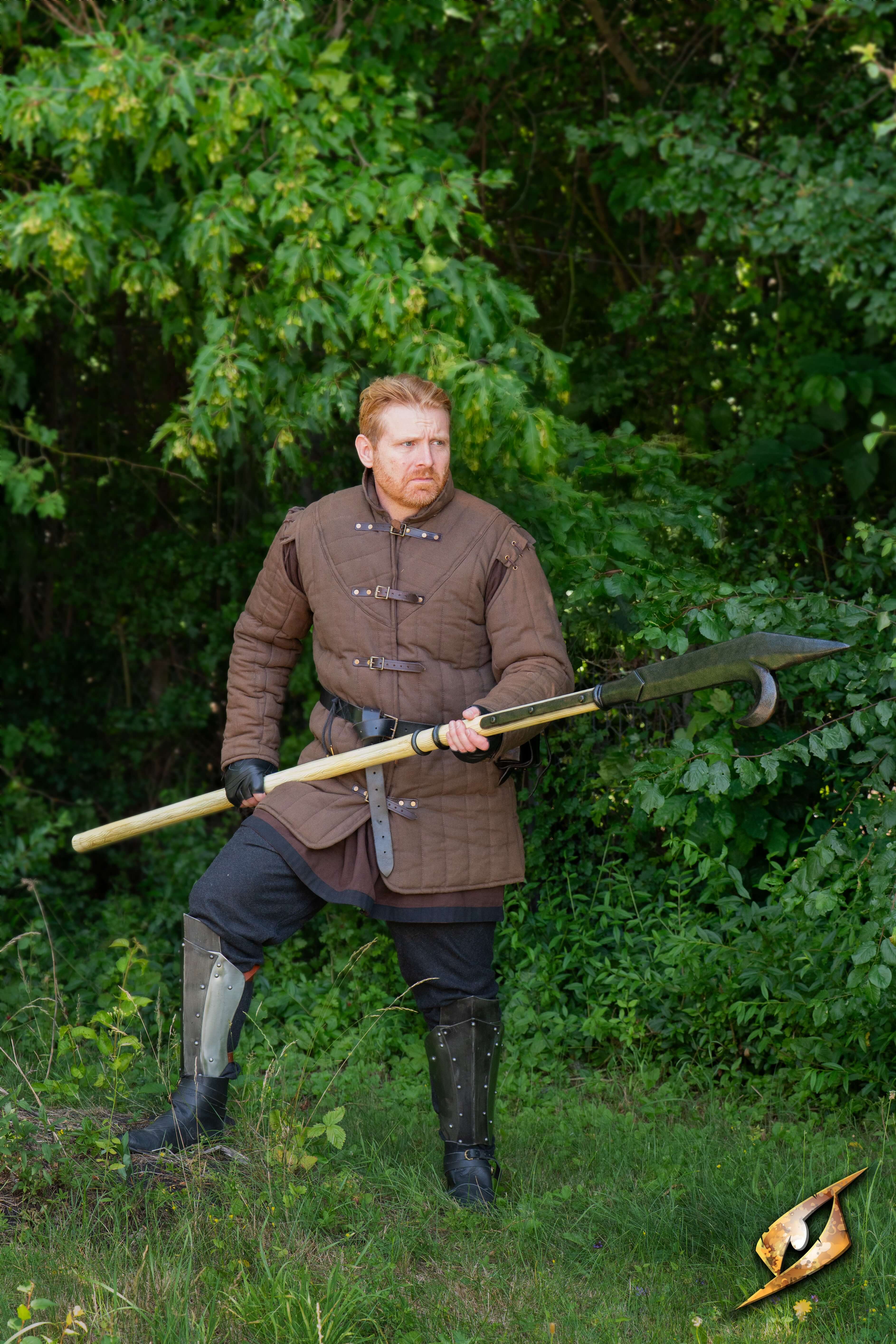 Man standing with a Bill Hook in a green forest, showcasing its design and usefulness in battle.