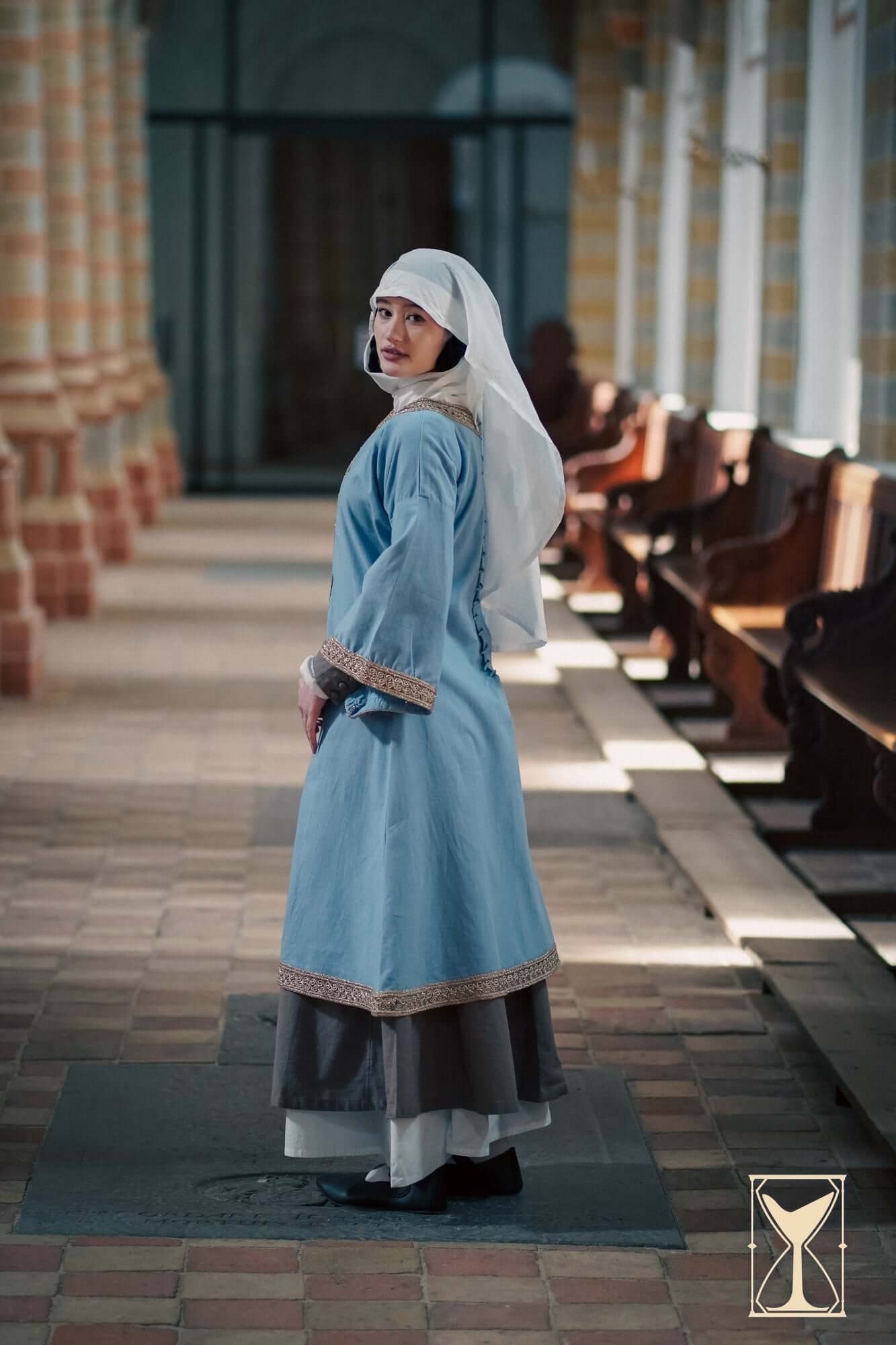 Overtunic Matilde worn by a model, showcasing wide sleeves and woven trim details in a historical setting.