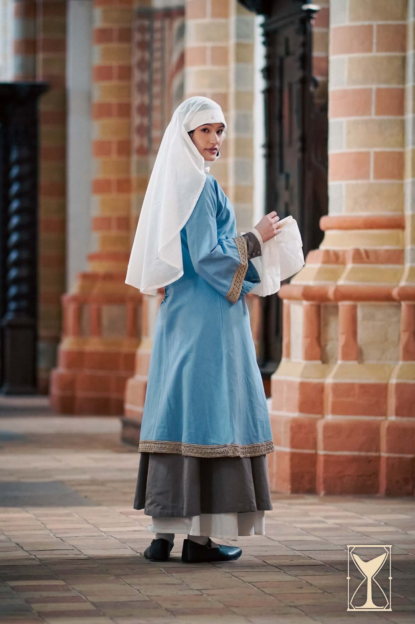 Overtunic Matilde model wearing historical tunic with wide sleeves and woven patterned trim in a medieval setting.