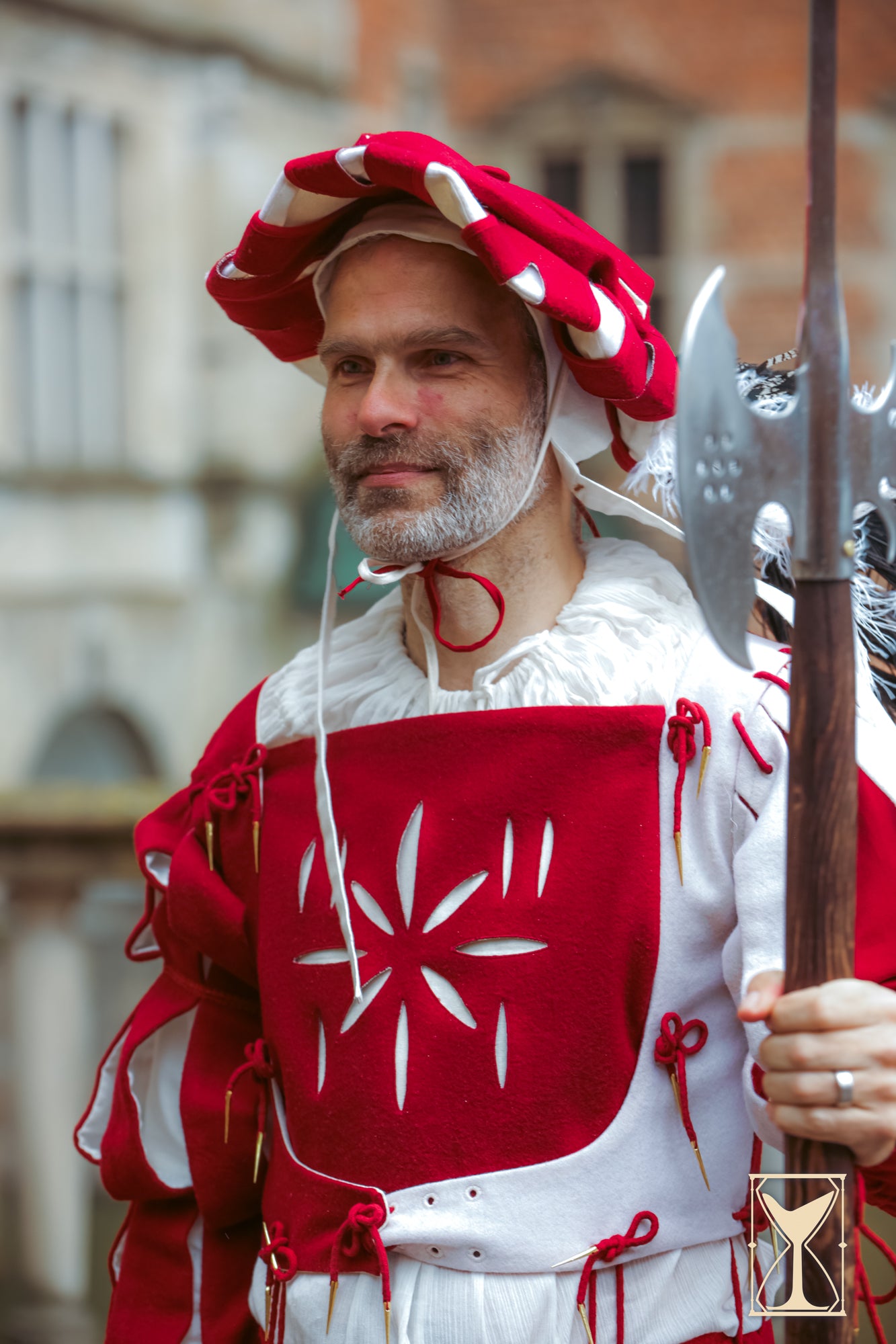 Man in historical reenactment costume with red and white attire, holding a spear.