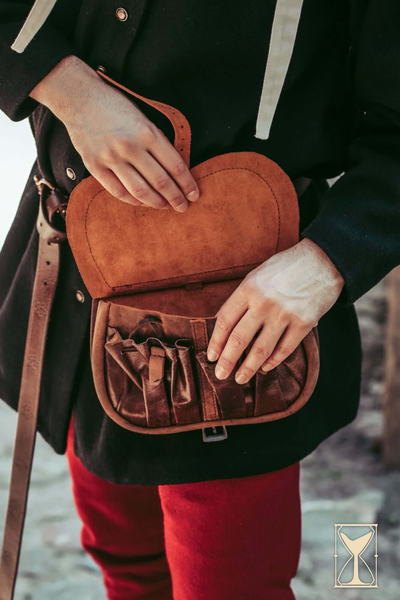 A person holding a Kidney Bag made of warm brown leather with an organized interior for practical use.