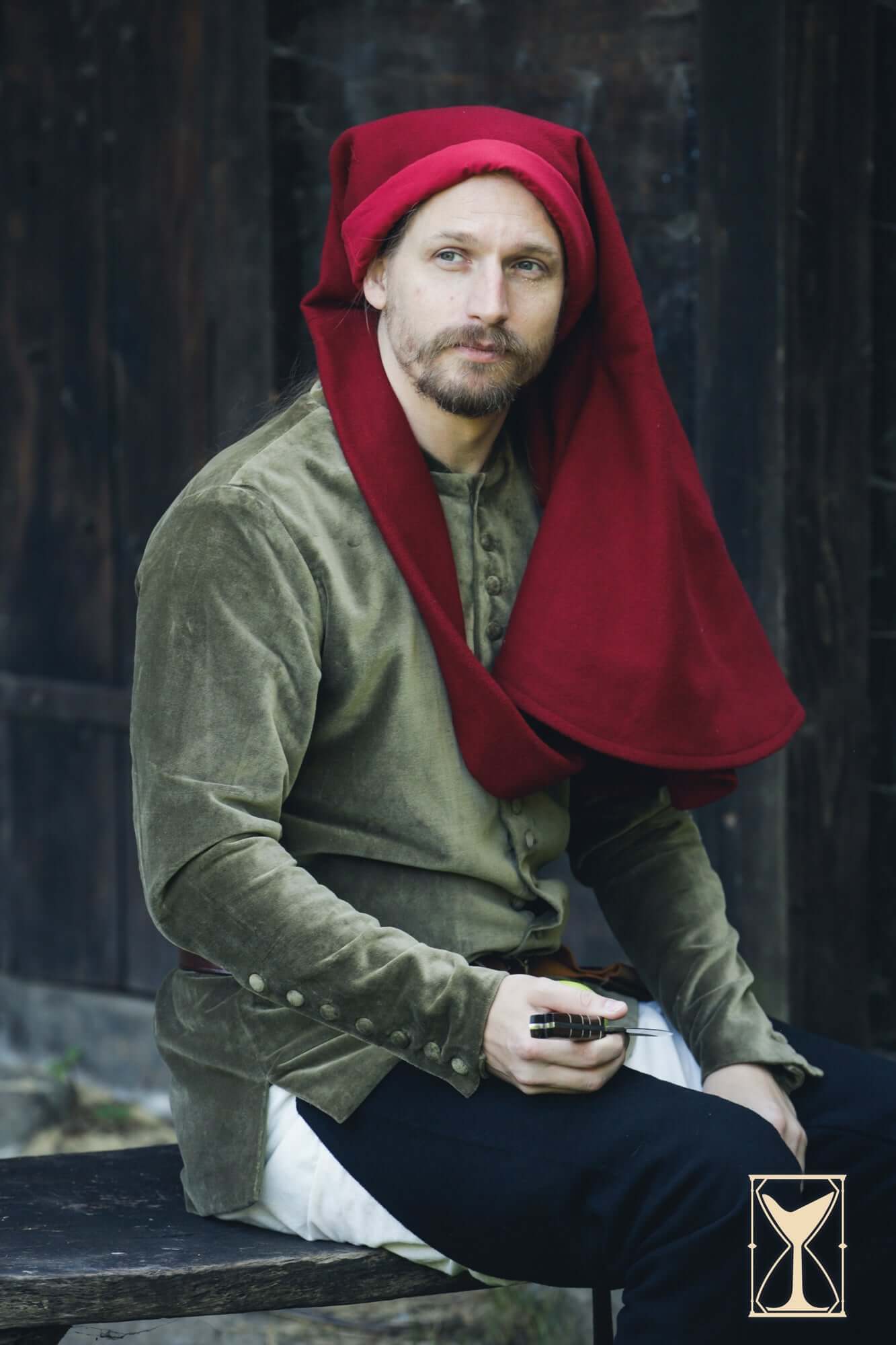 Man in a Cotehardie Bonifacio with red hood, sitting on a bench, showcasing historical attire.