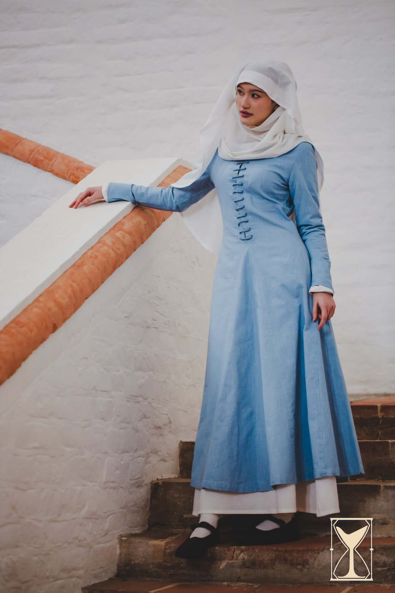 Cotehardie Marian dress in blue with central lacing showcased on a model near a staircase.