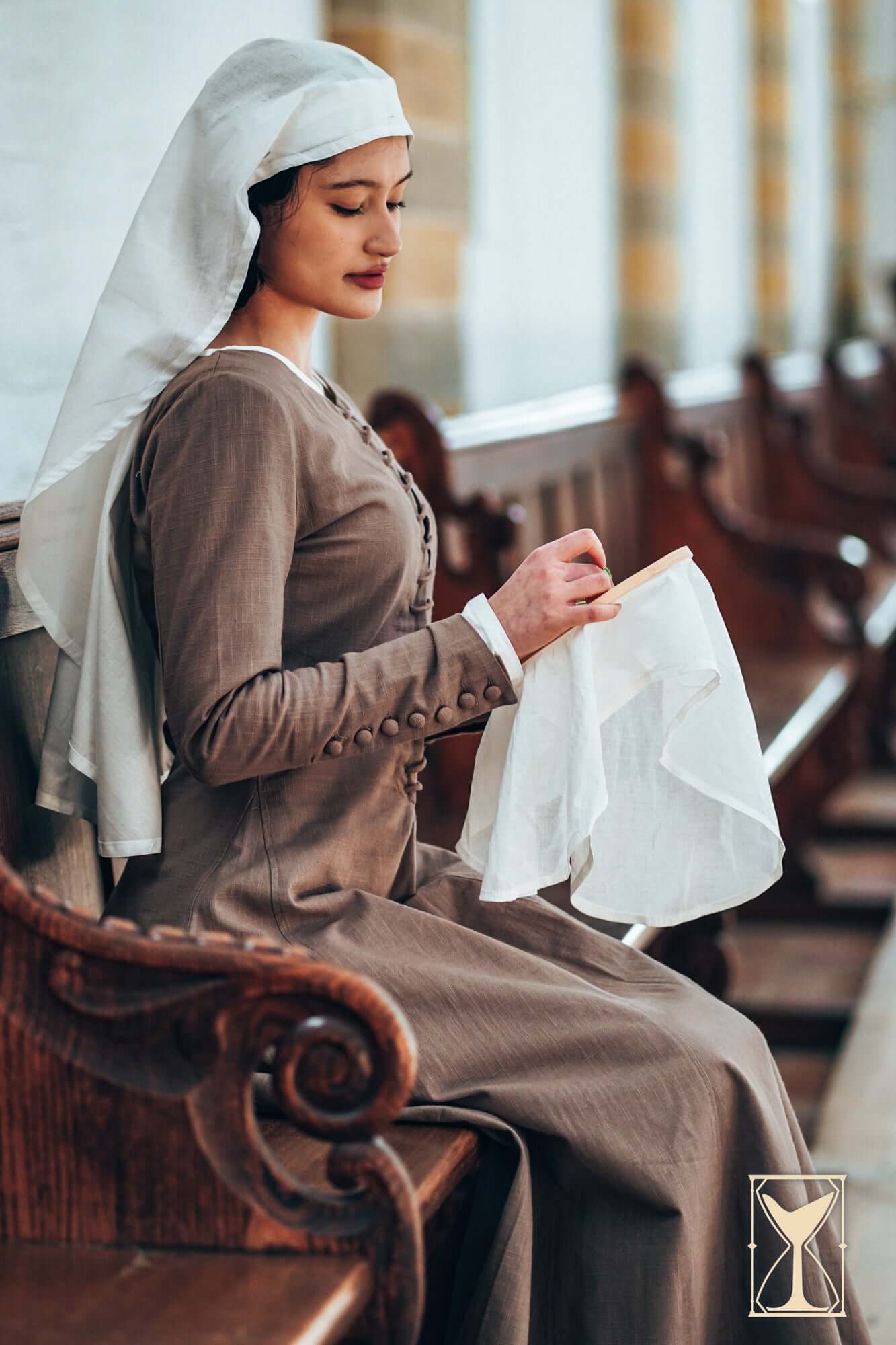 Cotehardie Marian dress worn by a woman seated, showcasing the fabric and lacing detail in a medieval setting.
