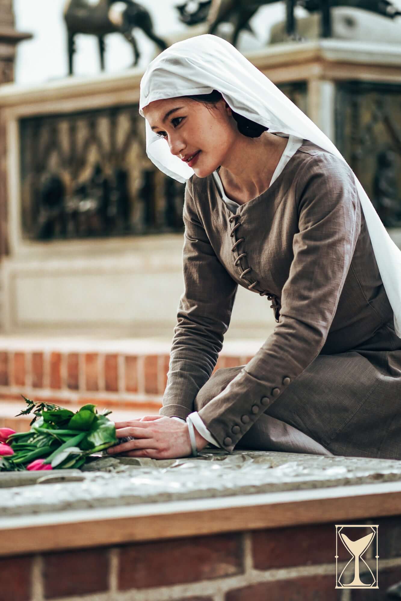 Cotehardie Marian dress displayed on a model arranging flowers, showcasing high medieval design with central lacing.