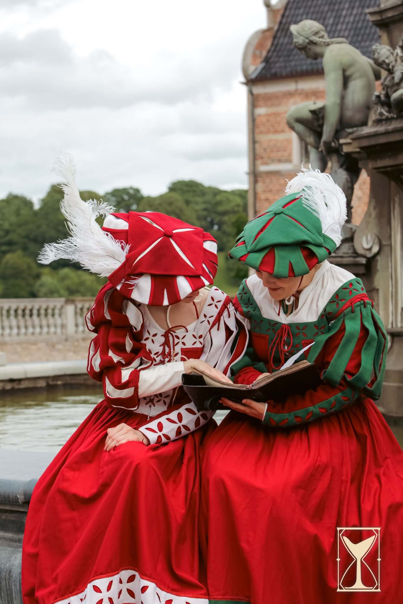 Landsknecht Hat: Two women in red and green layered hats and Renaissance dresses reading by a fountain.
