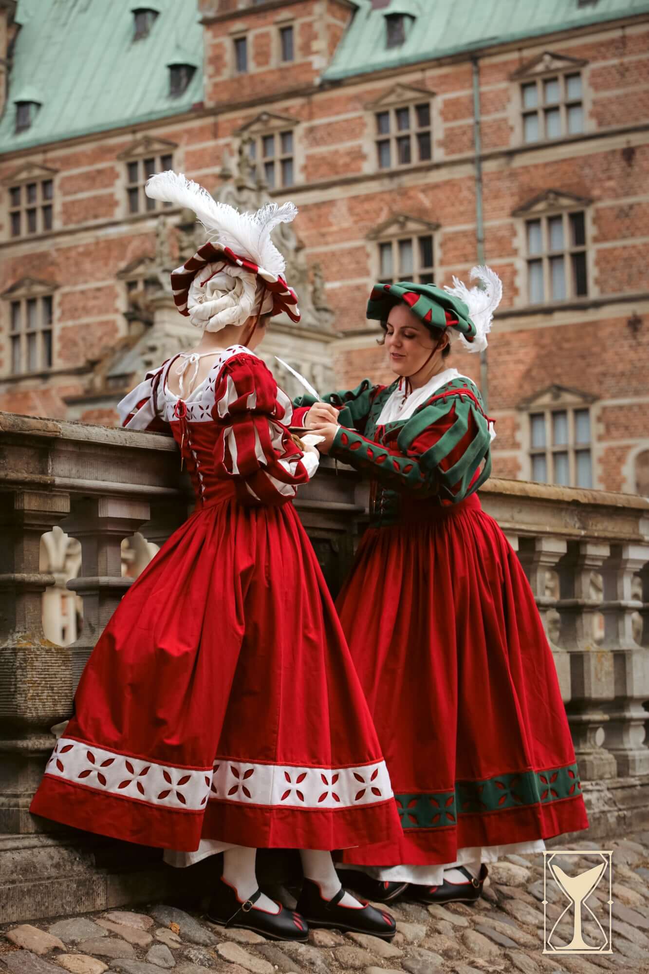 Two women in vibrant red Renaissance dresses with feathered hats, showcasing historical fashion elegance.